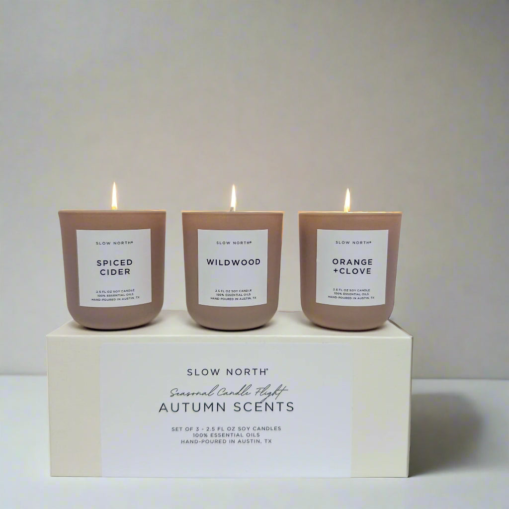 Three candles with labels 'Spiced Cider', 'Wildwood', and 'Orange Clove' on a box labeled 'Slow North'.