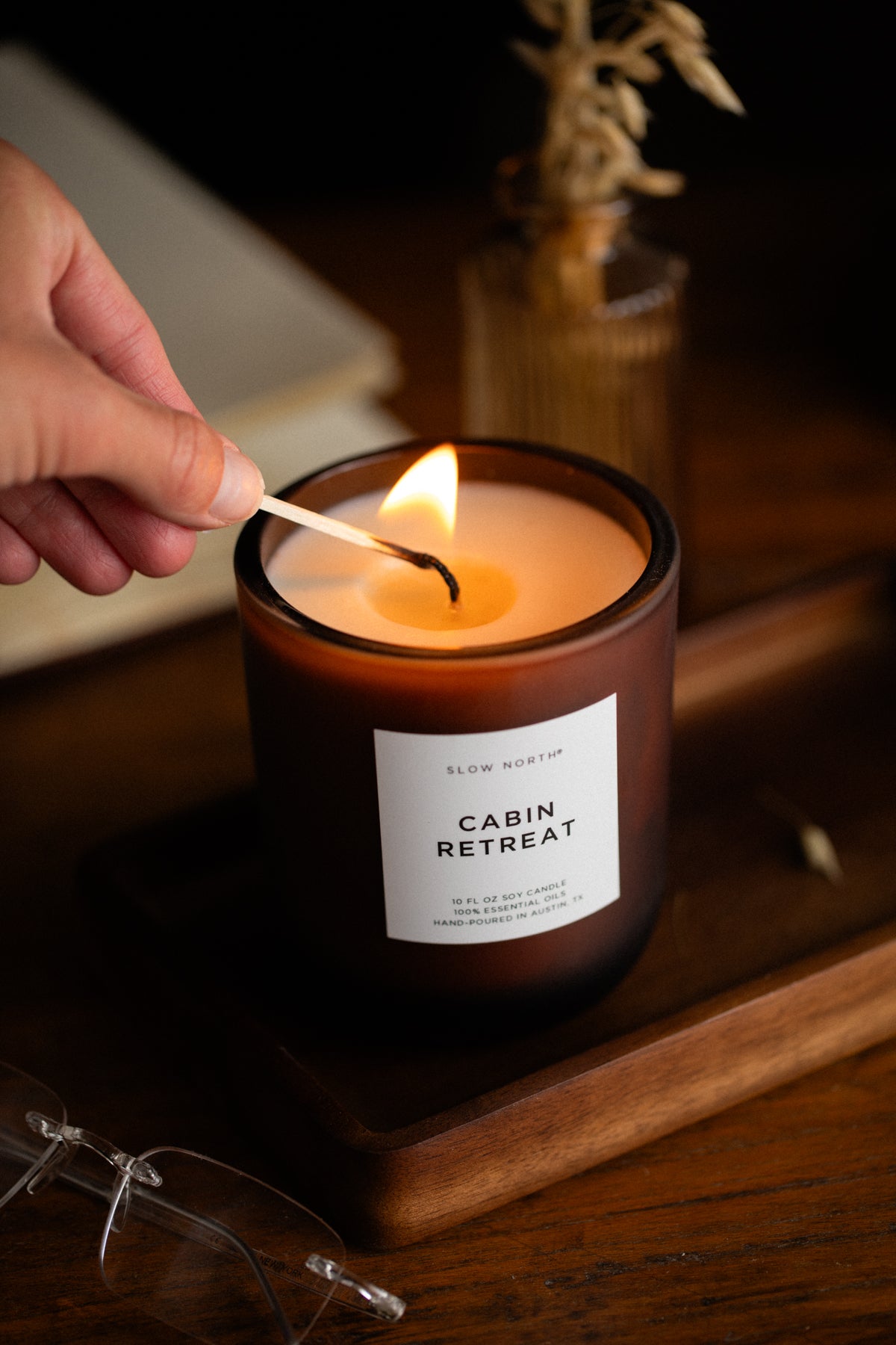 Candle labeled 'Cabin Retreat' being lit with a match on a wooden surface.