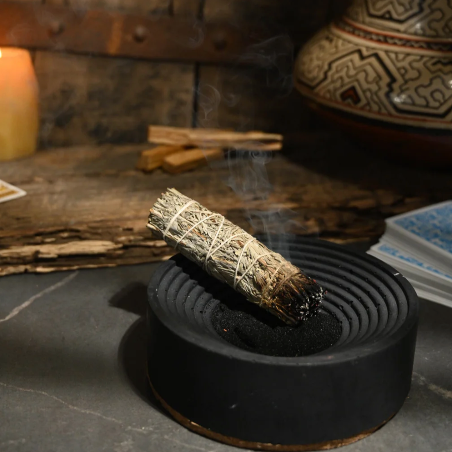 Smoldering sage stick in a black holder on a stone surface with a rustic background.