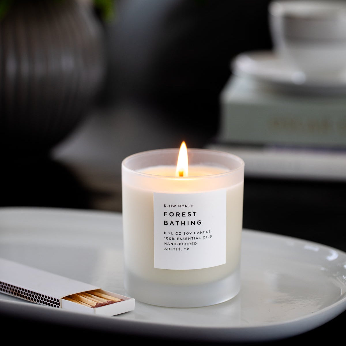 Candle labeled 'Forest Bathing' on a white plate with a blurred background