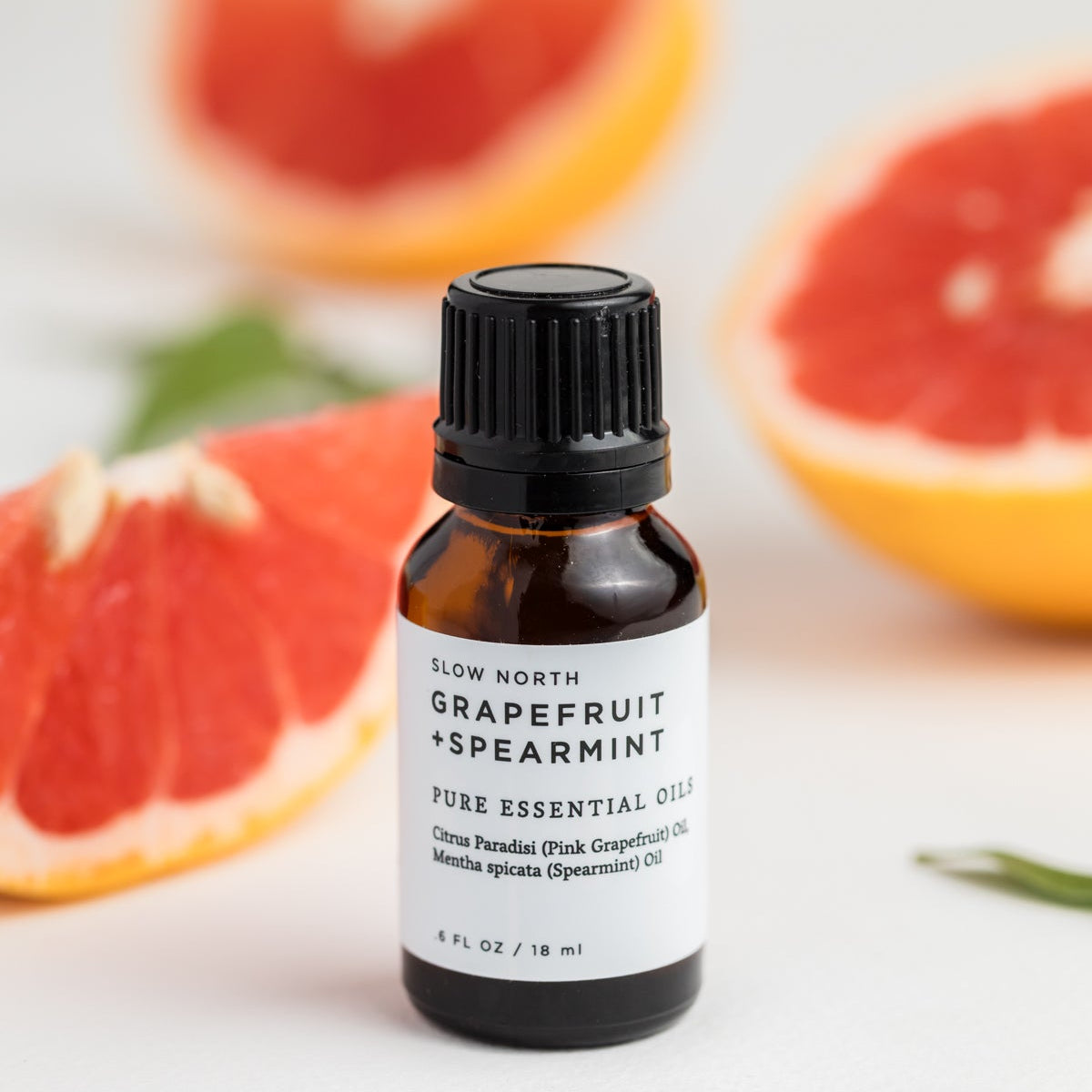Bottle of grapefruit spearmint essential oil with grapefruit slices in the background