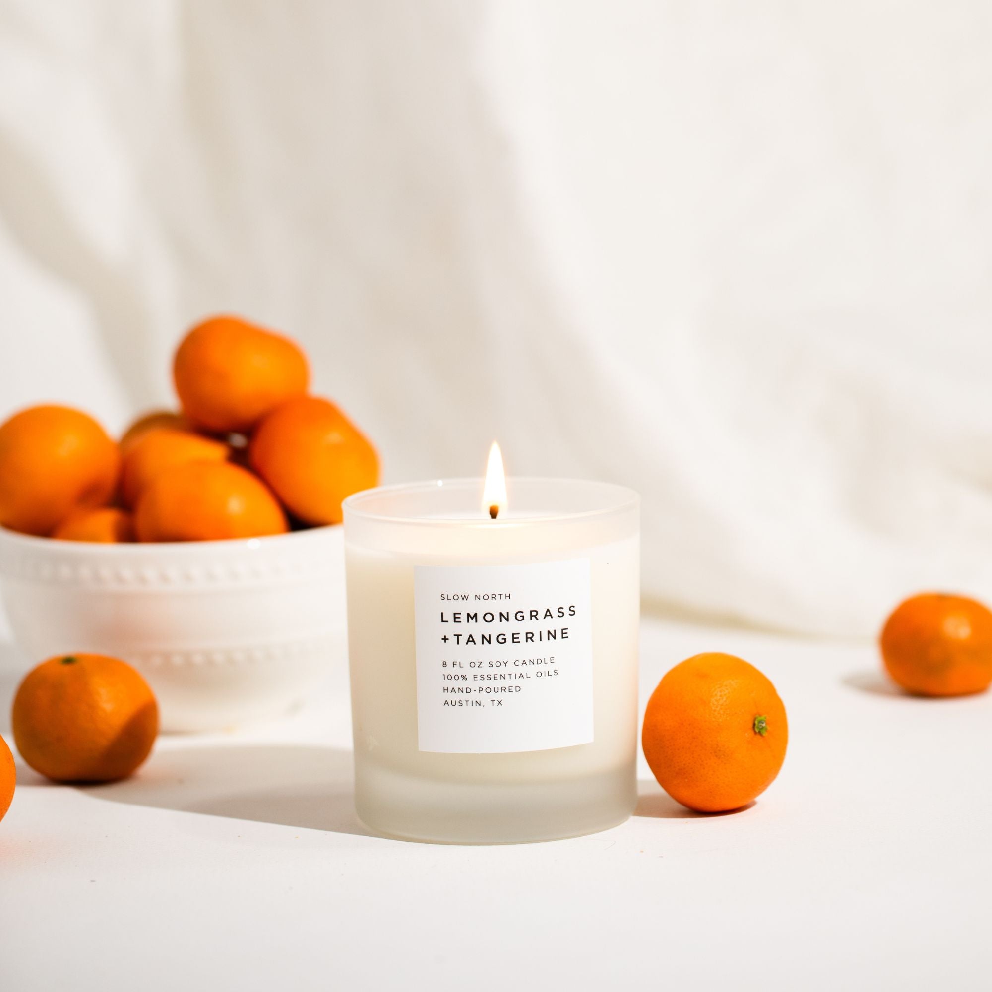 Candle labeled 'Lemongrass + Tangerine' with oranges on a white background