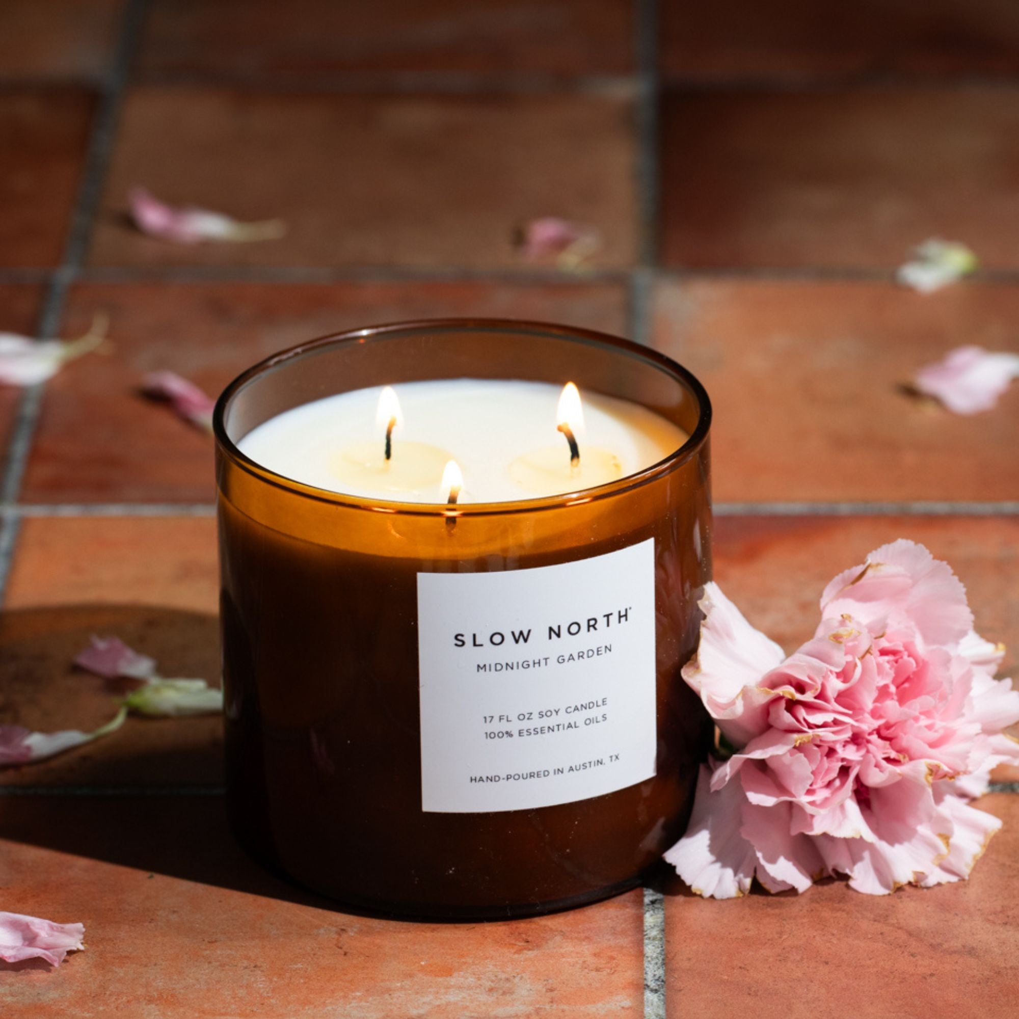 Scented candle with a label 'Slow North' on a tiled surface with pink flowers.