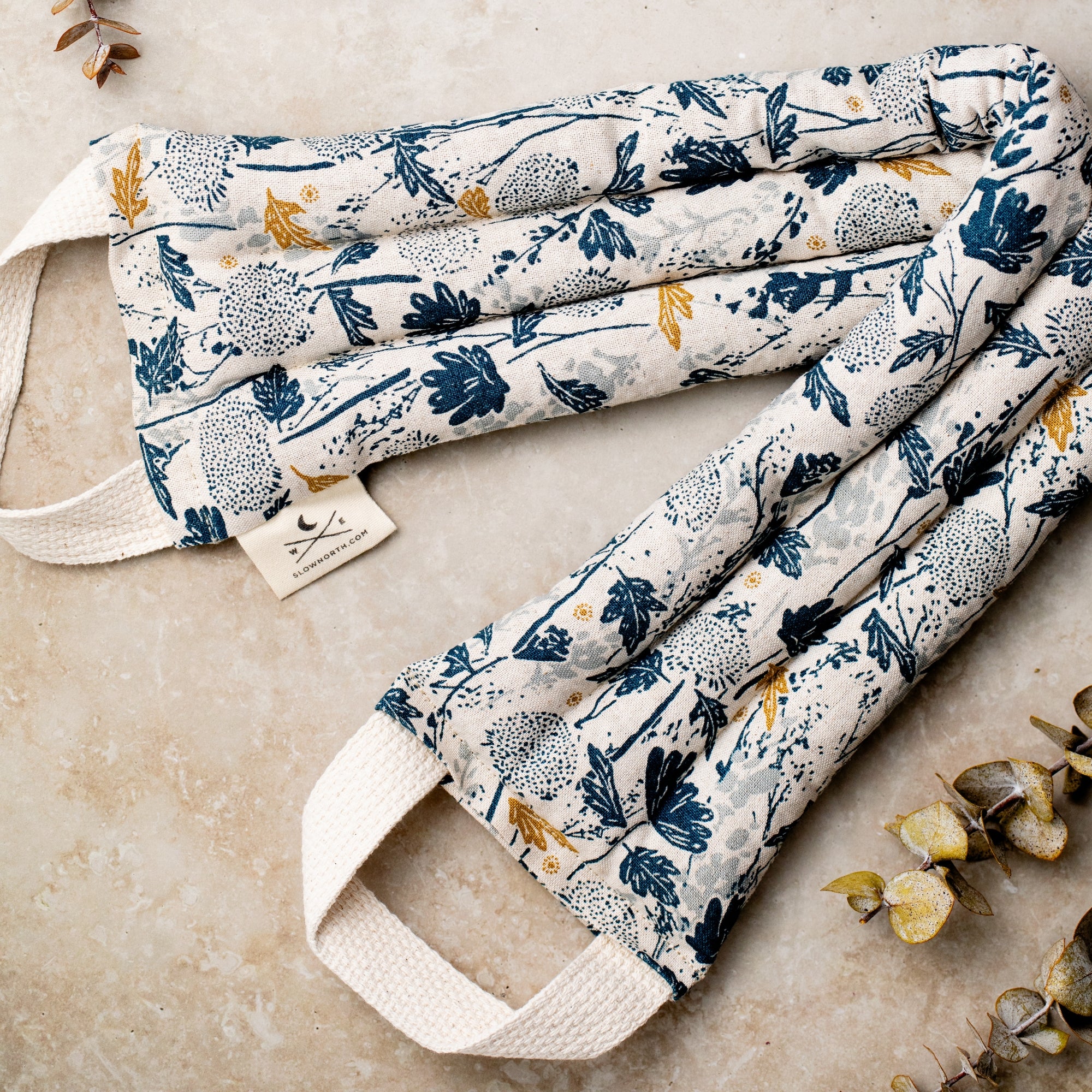 Floral-patterned fabric neck wrap with handles on a neutral background