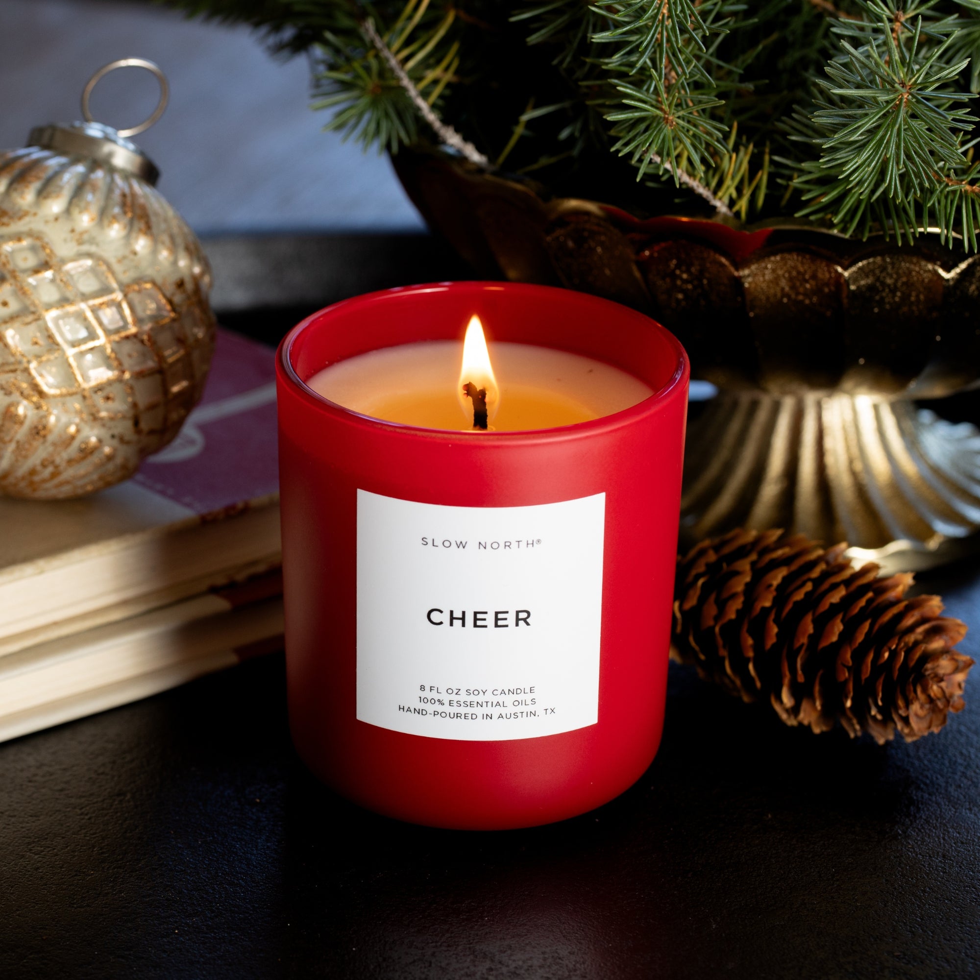 Red candle labeled 'CHEER' with a Christmas tree and decorations in the background