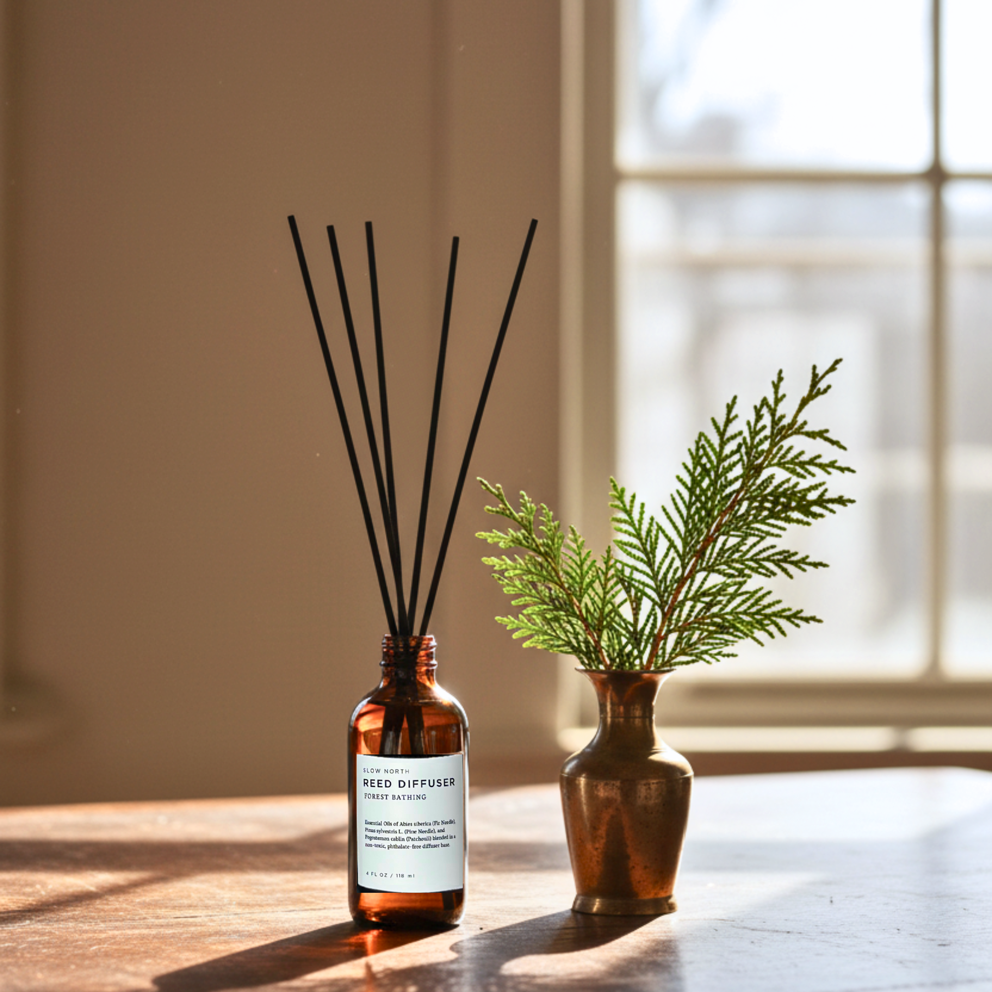 Reed diffuser with black reeds and a small vase with greenery on a wooden surface.