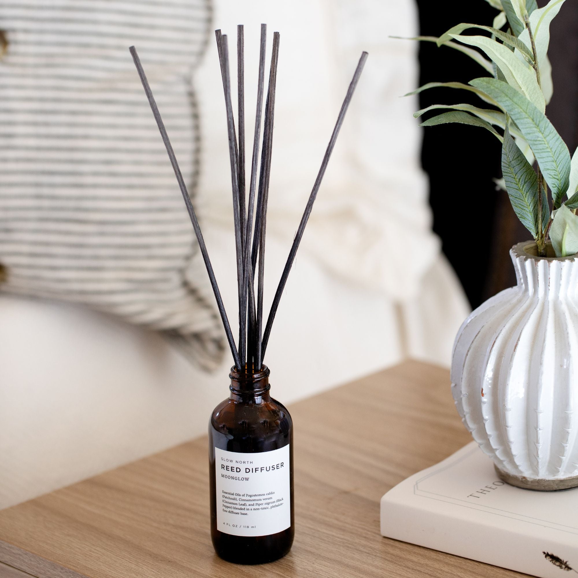 Reed diffuser with black sticks in a bottle on a wooden surface with a blurred background