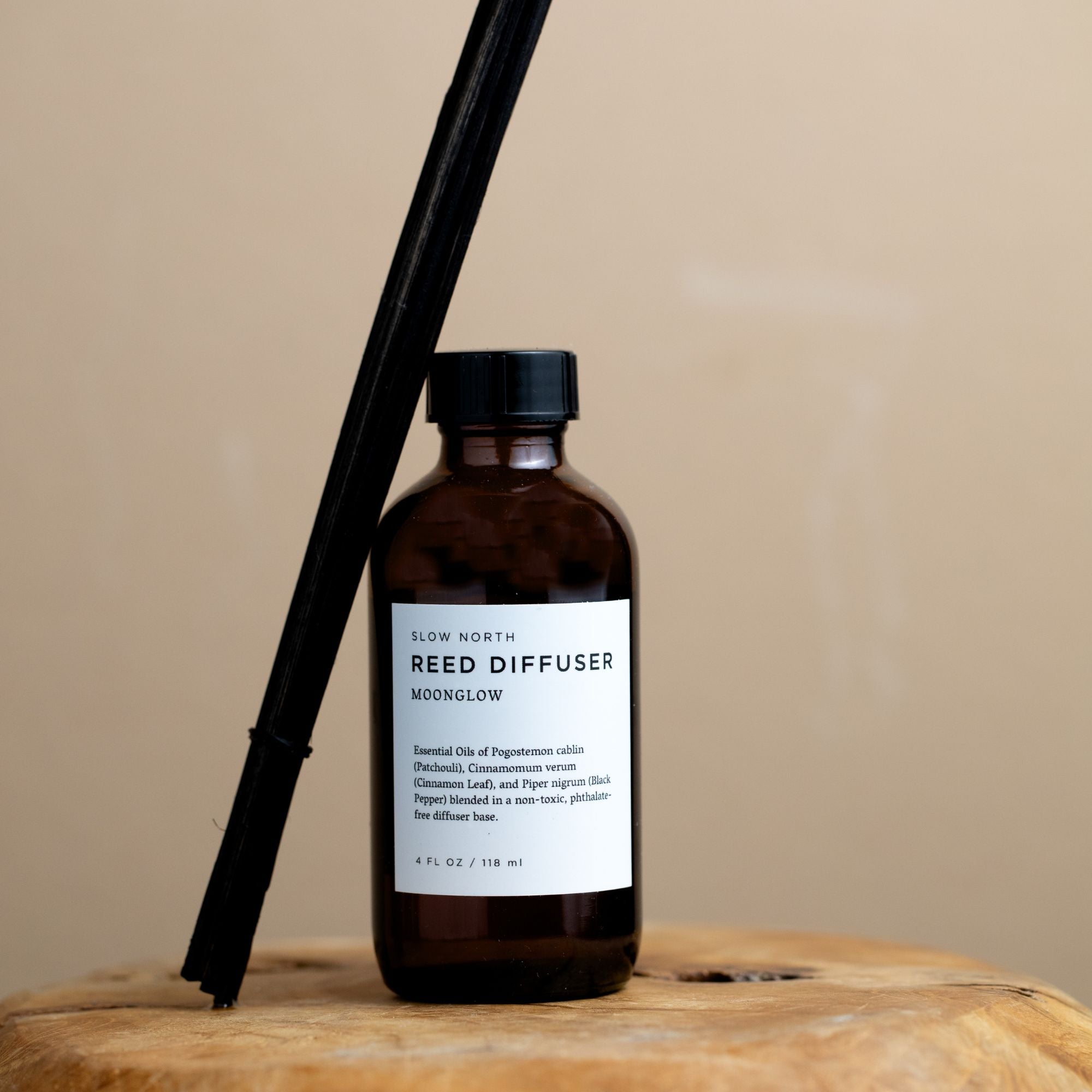Reed diffuser bottle with black reeds on a wooden surface against a beige background