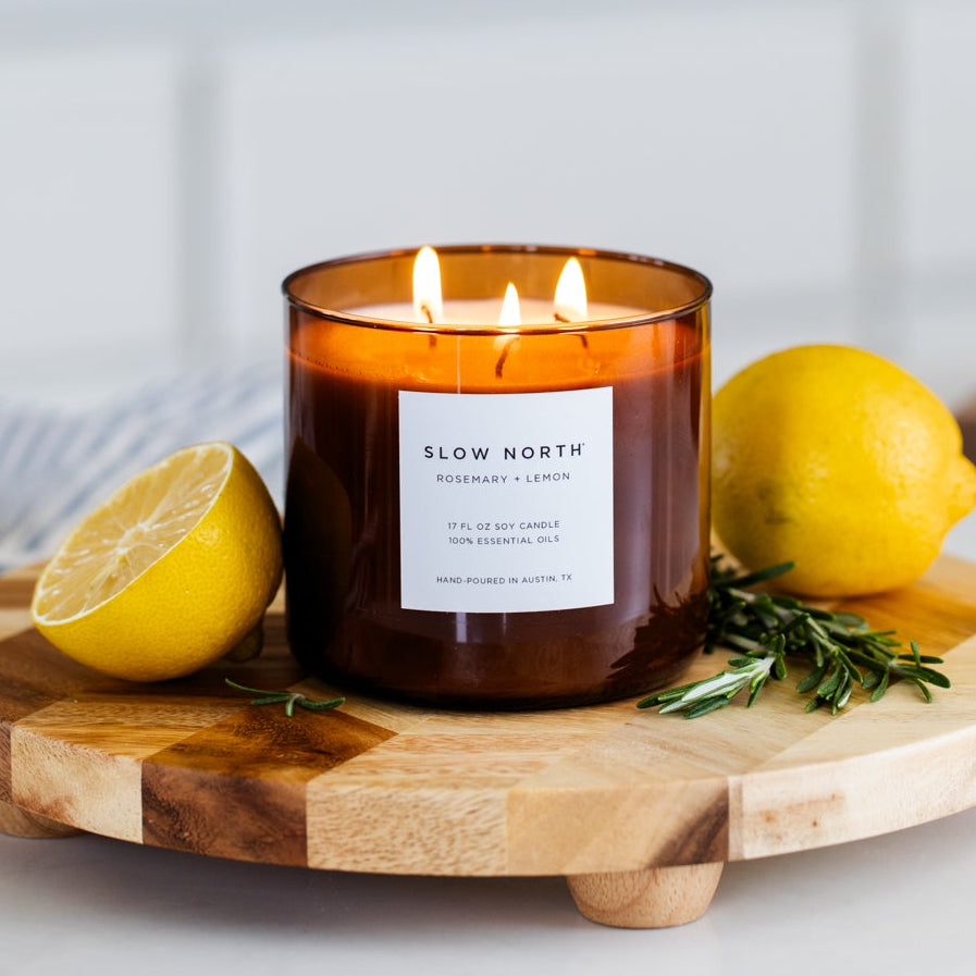 Candle with a label on a wooden cutting board with lemons and rosemary in a kitchen setting