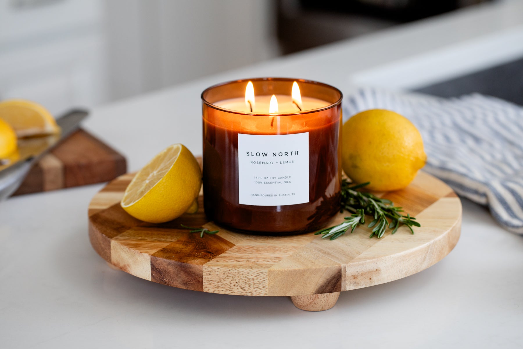 Candle with 'Slow North' label on a wooden board with lemons and rosemary.