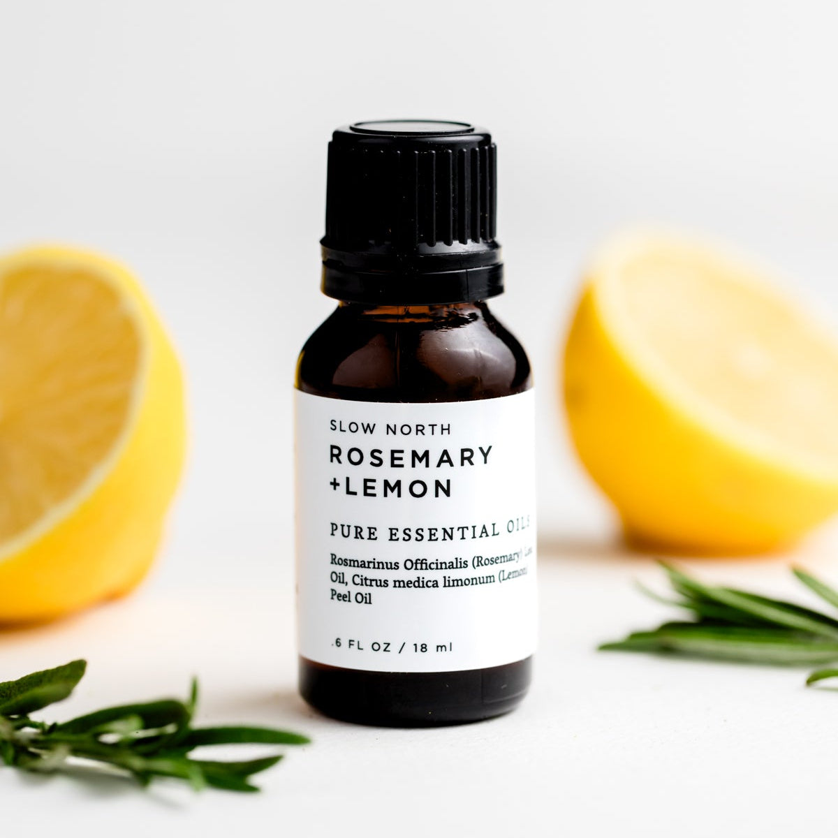 Bottle of Slow North Rosemary + Lemon essential oil with lemons and rosemary on a white background