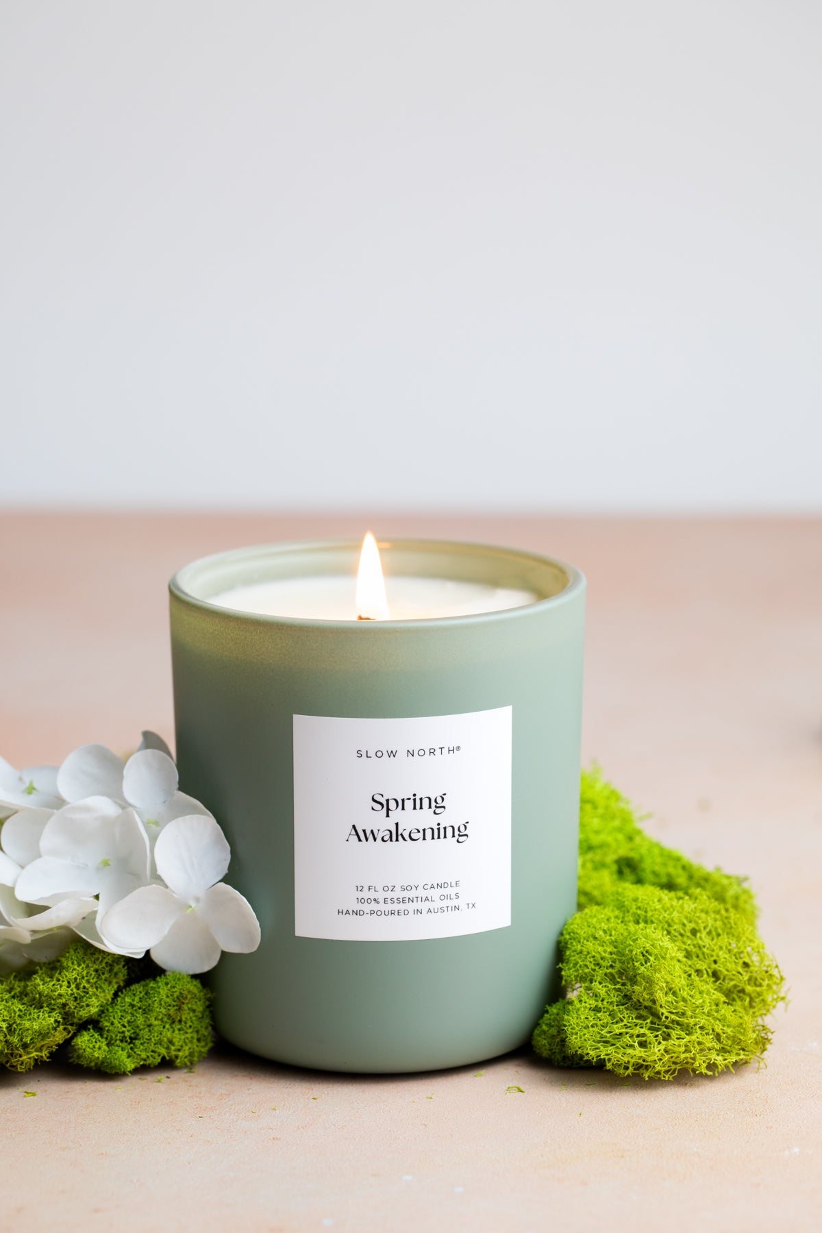Candle labeled 'Spring Awakening' with floral and moss decorations on a light background