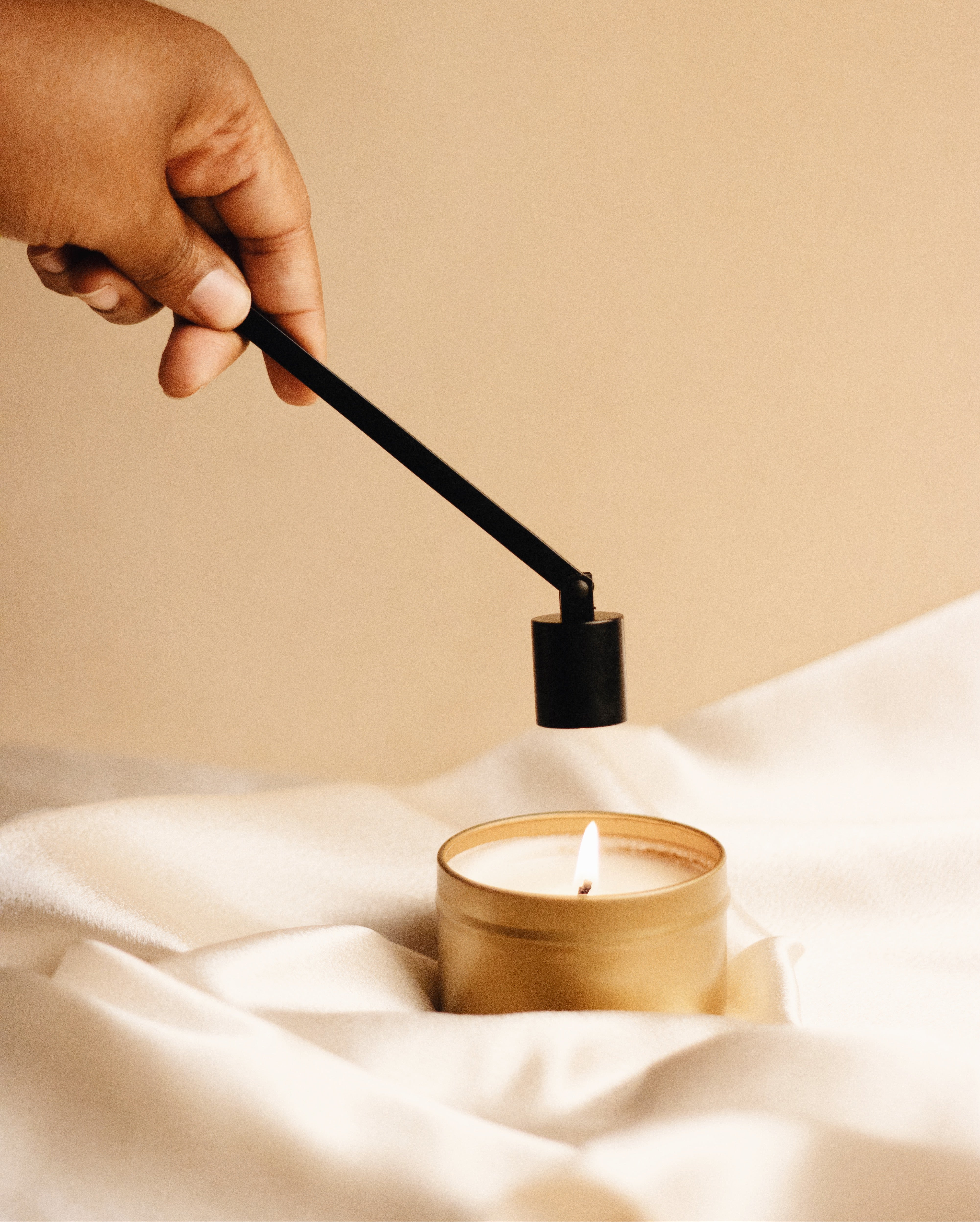 Hand holding candle snuffer over 6 ounce gold tin candle by Slow North