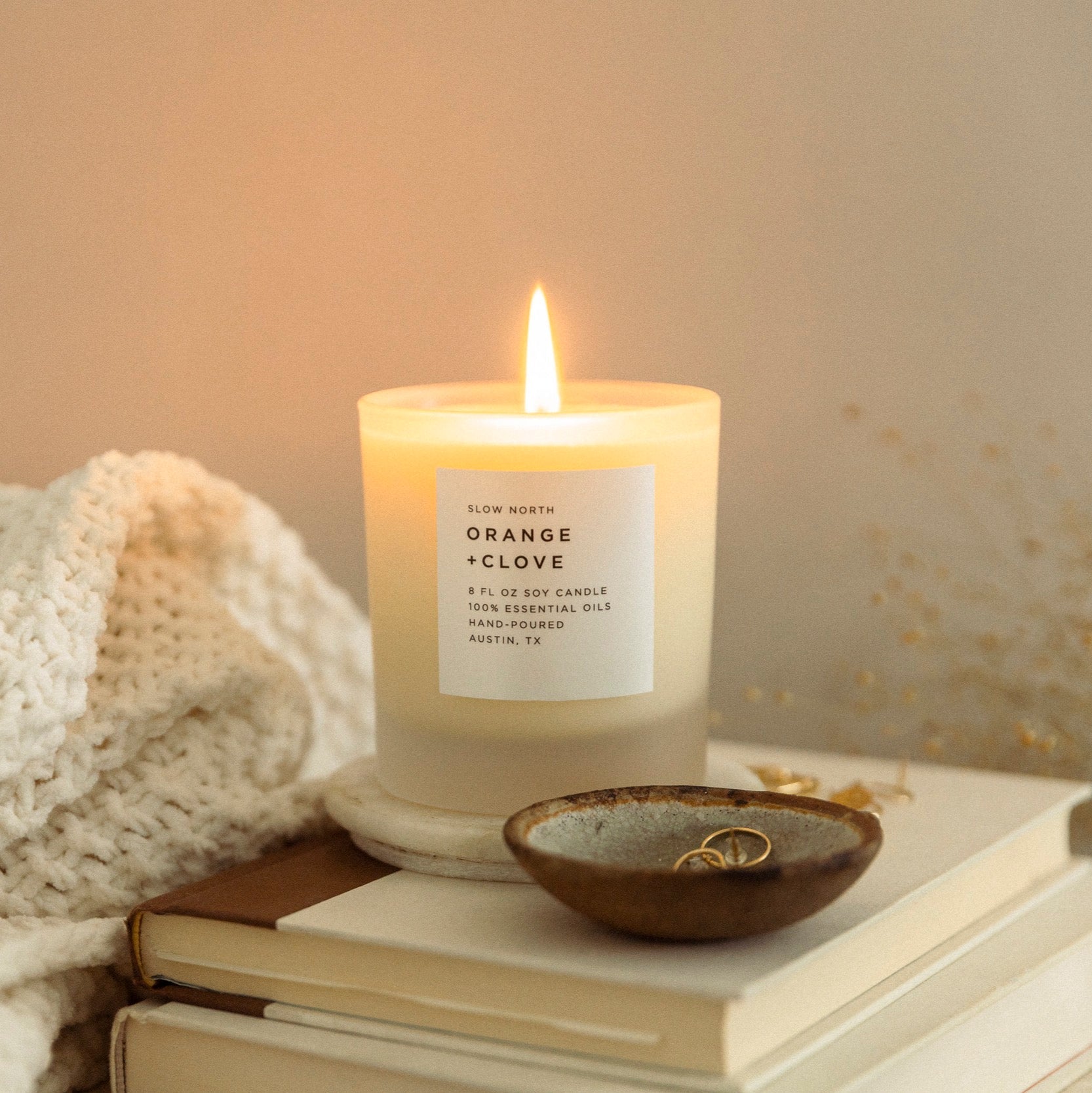lit candle next on a stack of books behind a brown ring dish