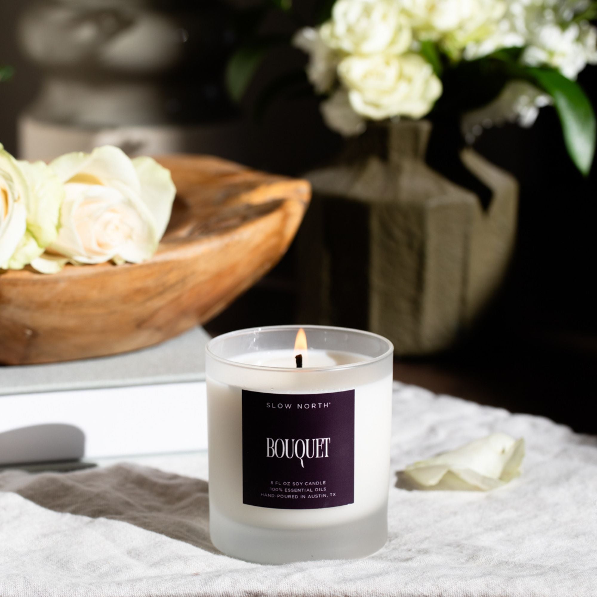 Candle with a 'Bouquet' label on a table with flowers in the background