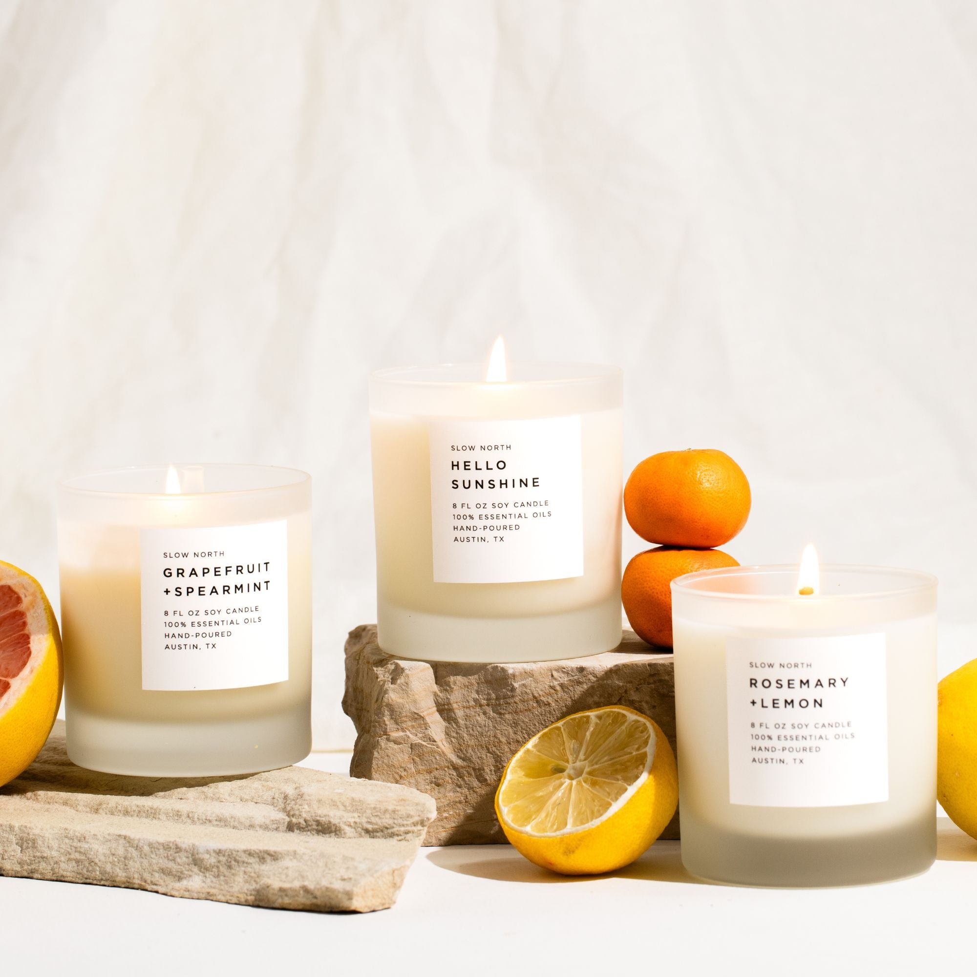 Three candles with labels surrounded by citrus fruits on a light background