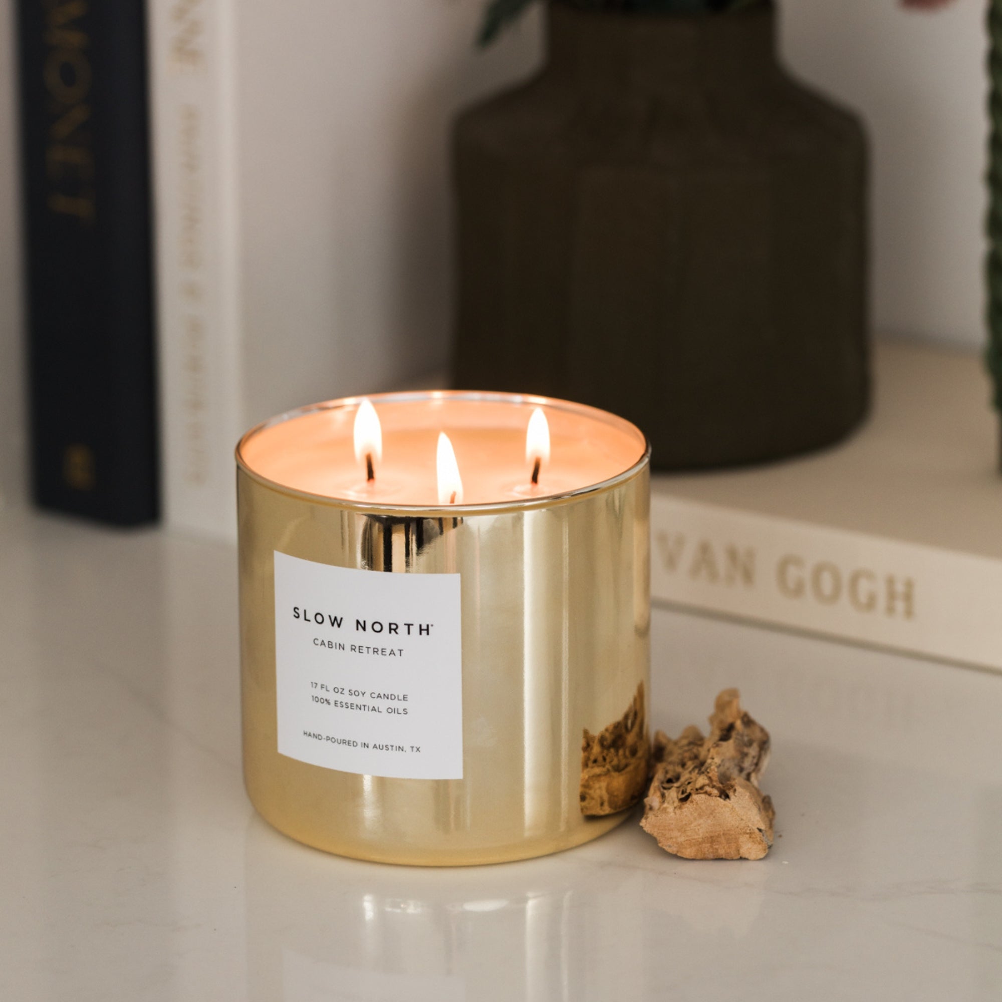 Gold candle with a label on a surface, with books and a vase in the background