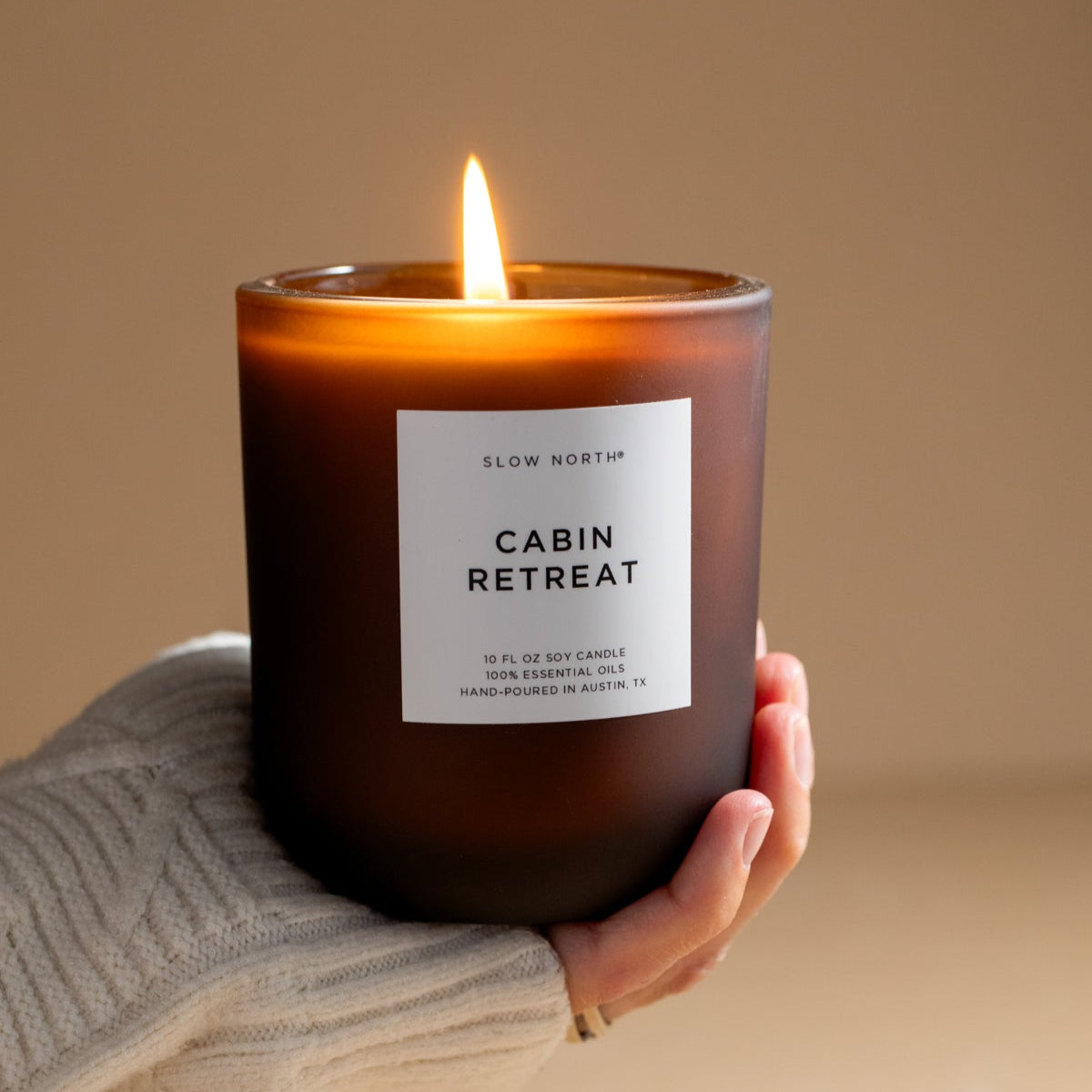 Candle labeled 'Cabin Retreat' held by a hand against a beige background