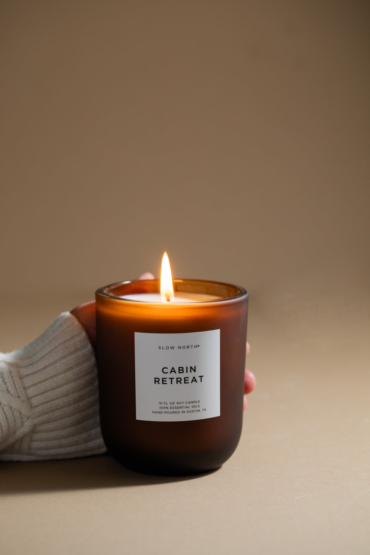 Candle labeled 'Cabin Retreat' held by a person wearing a white sweater against a beige background