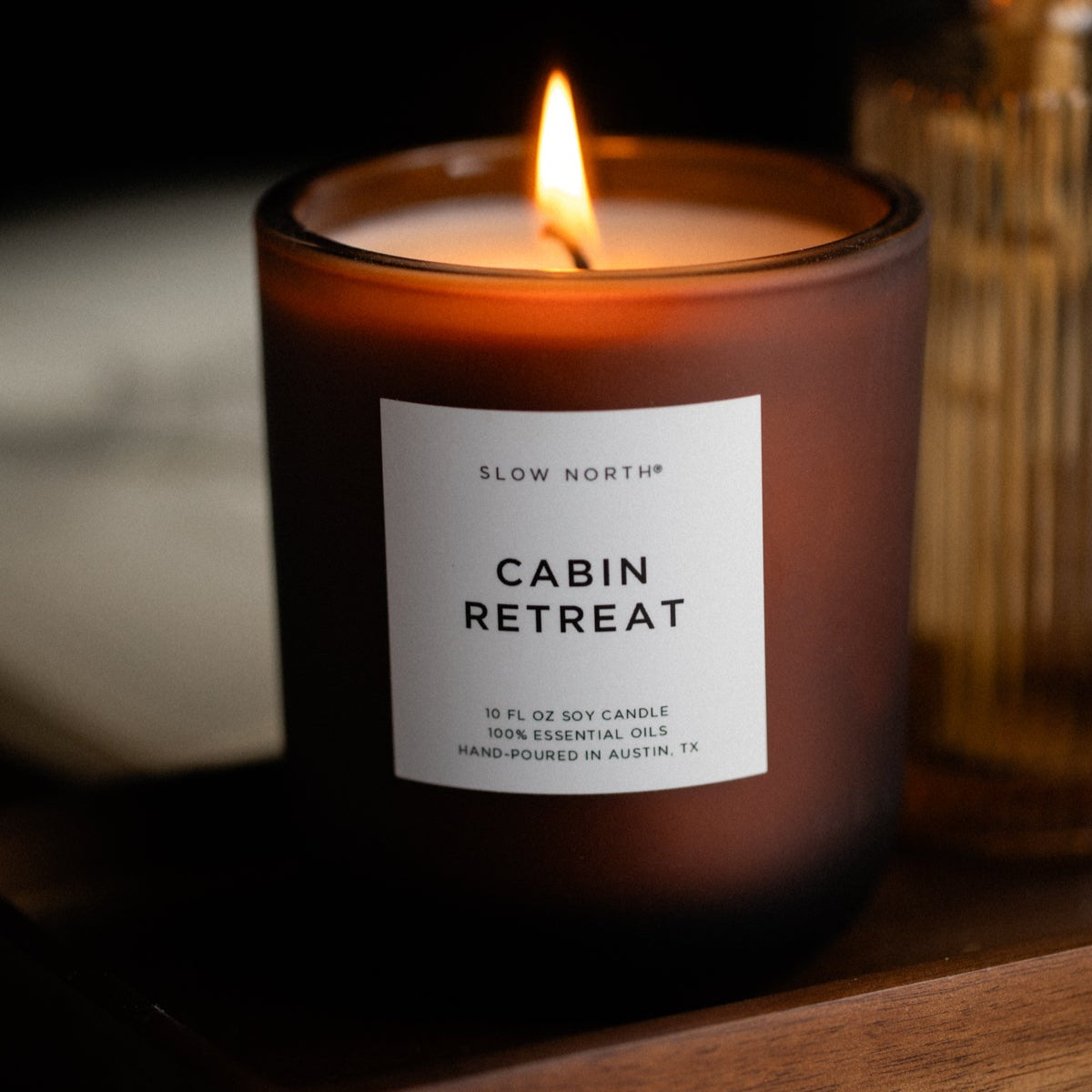 Candle labeled 'Cabin Retreat' by Slow North on a wooden surface with a dark background.