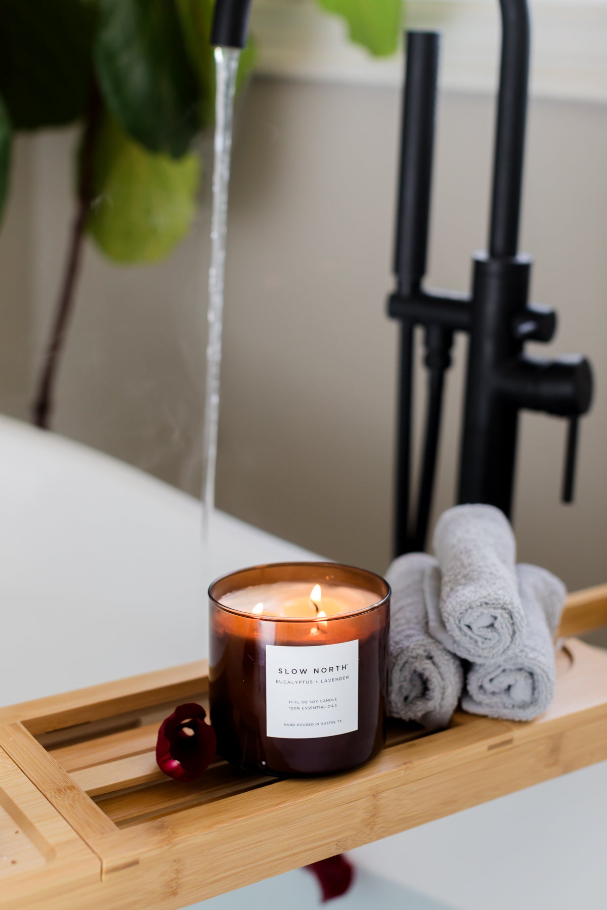 Candle on a bath tray with towels and a faucet in the background