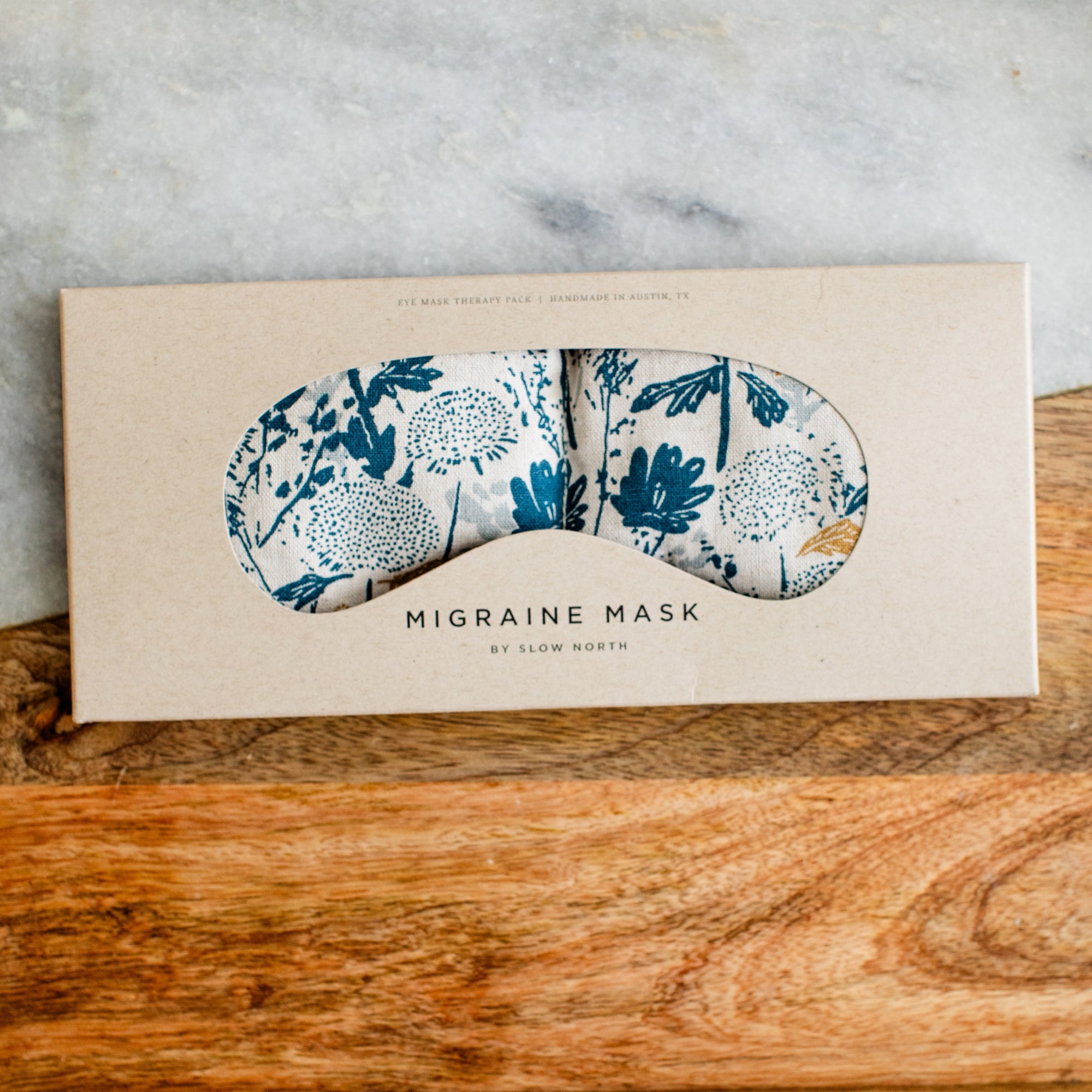 Migraine mask with blue floral pattern in a beige box on a wooden surface.