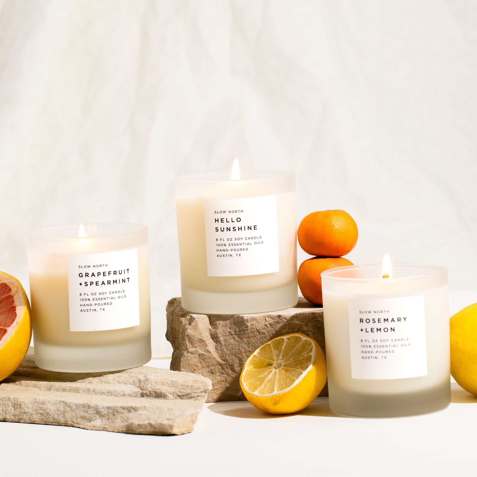 Three candles with labels on a white surface with fruits and paper.