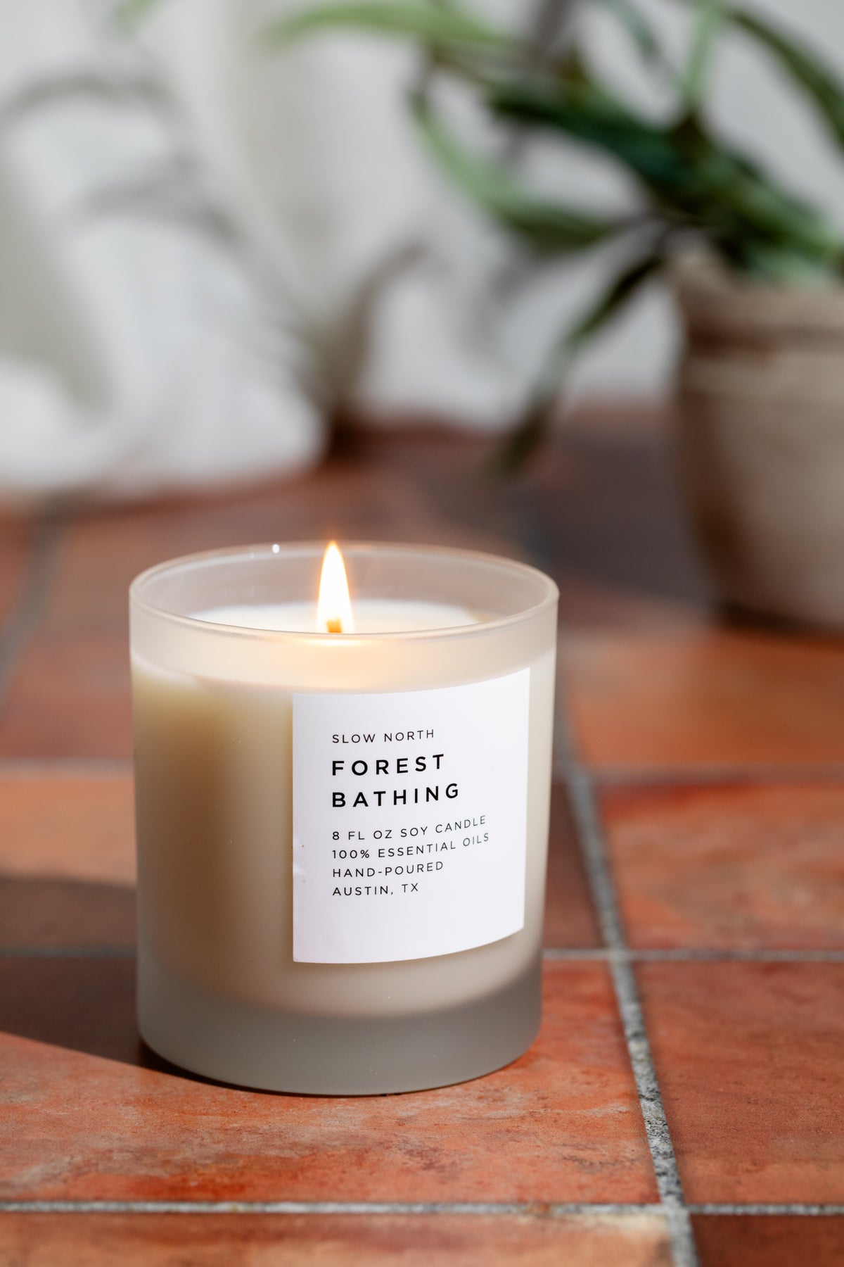 Candle labeled 'Forest Bathing' on a tiled surface with a plant in the background