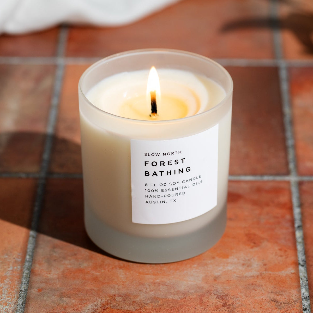 Candle labeled 'Forest Bathing' on a tiled floor