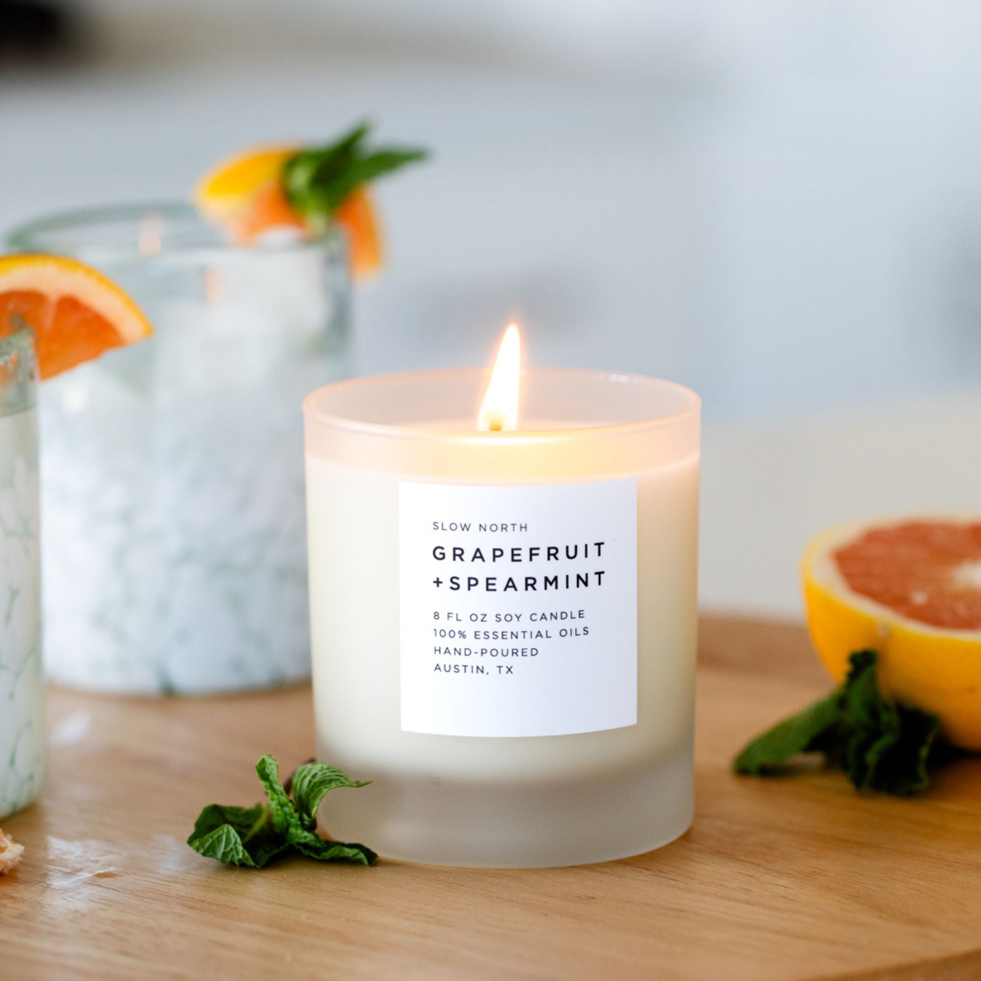 Grapefruit and spearmint candle on a wooden surface with citrus fruits and a blurred background