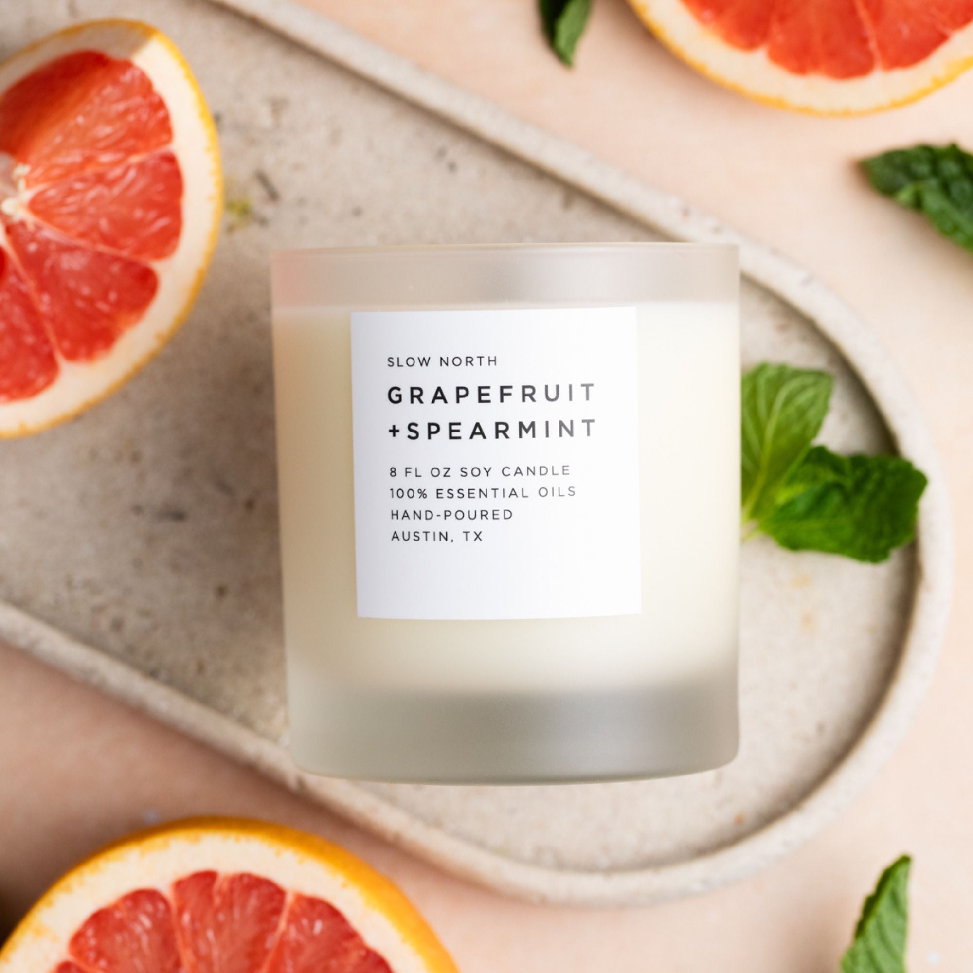 Grapefruit and spearmint candle with sliced grapefruits and mint leaves on a stone surface