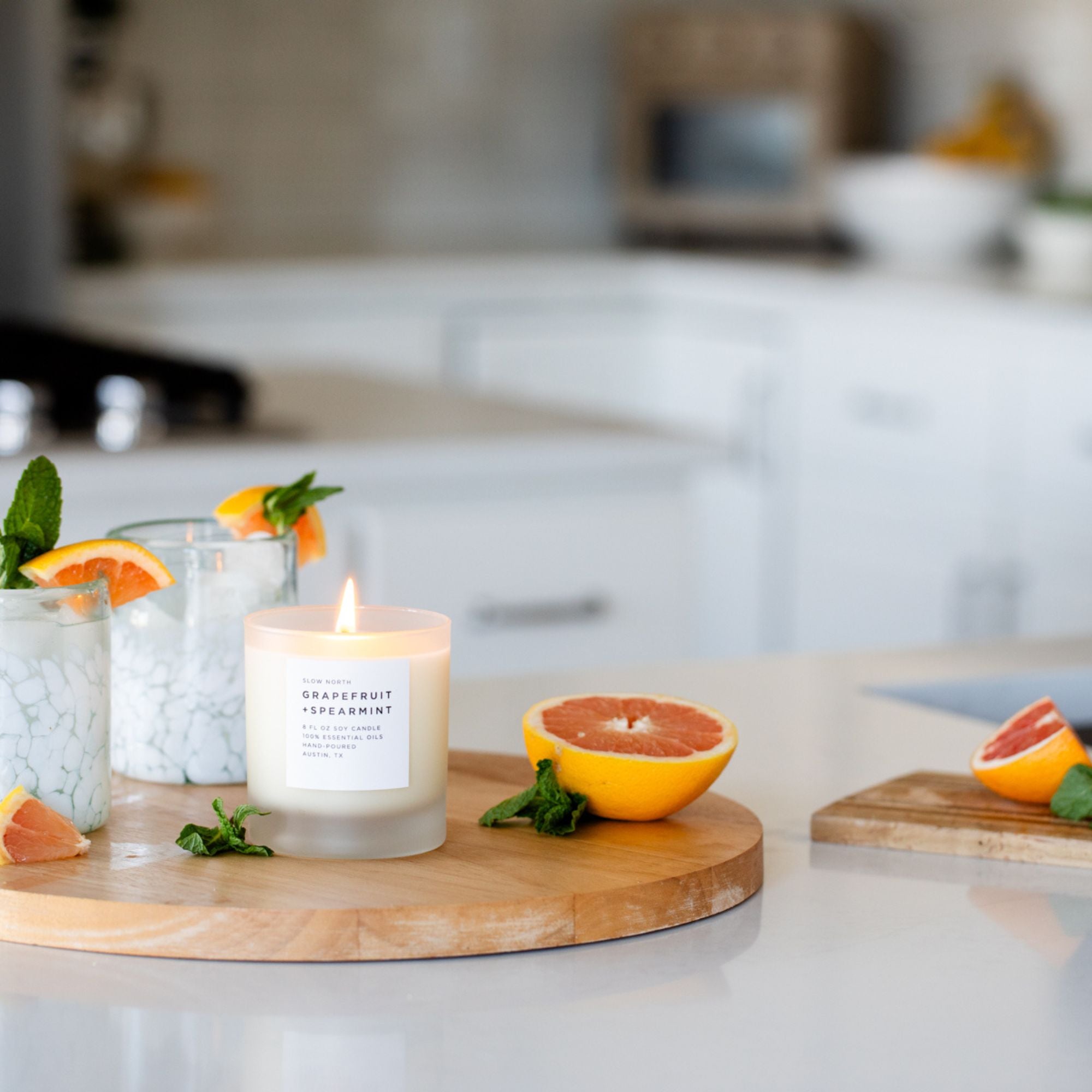 Candle on a wooden board with grapefruit and mint leaves in a kitchen setting