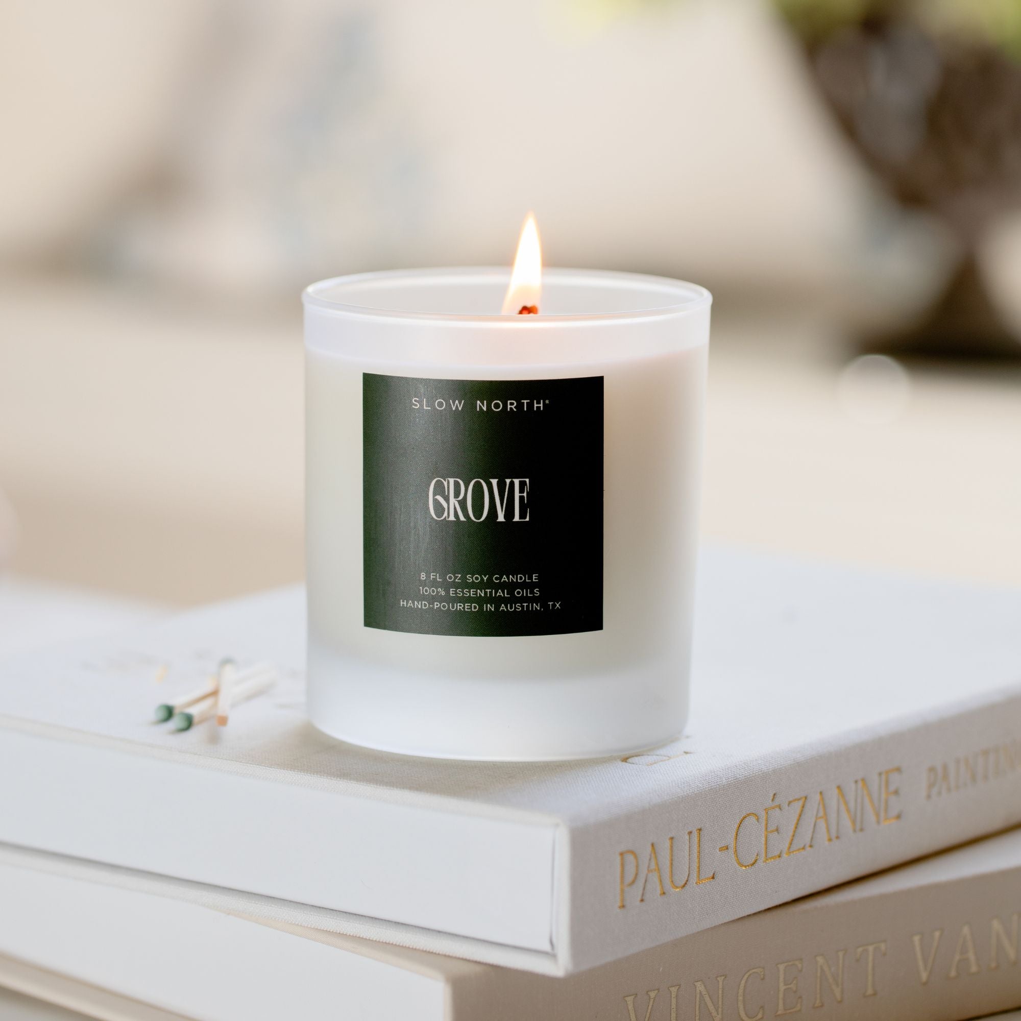 Candle labeled 'Grove' from Slow North on a book with a blurred background