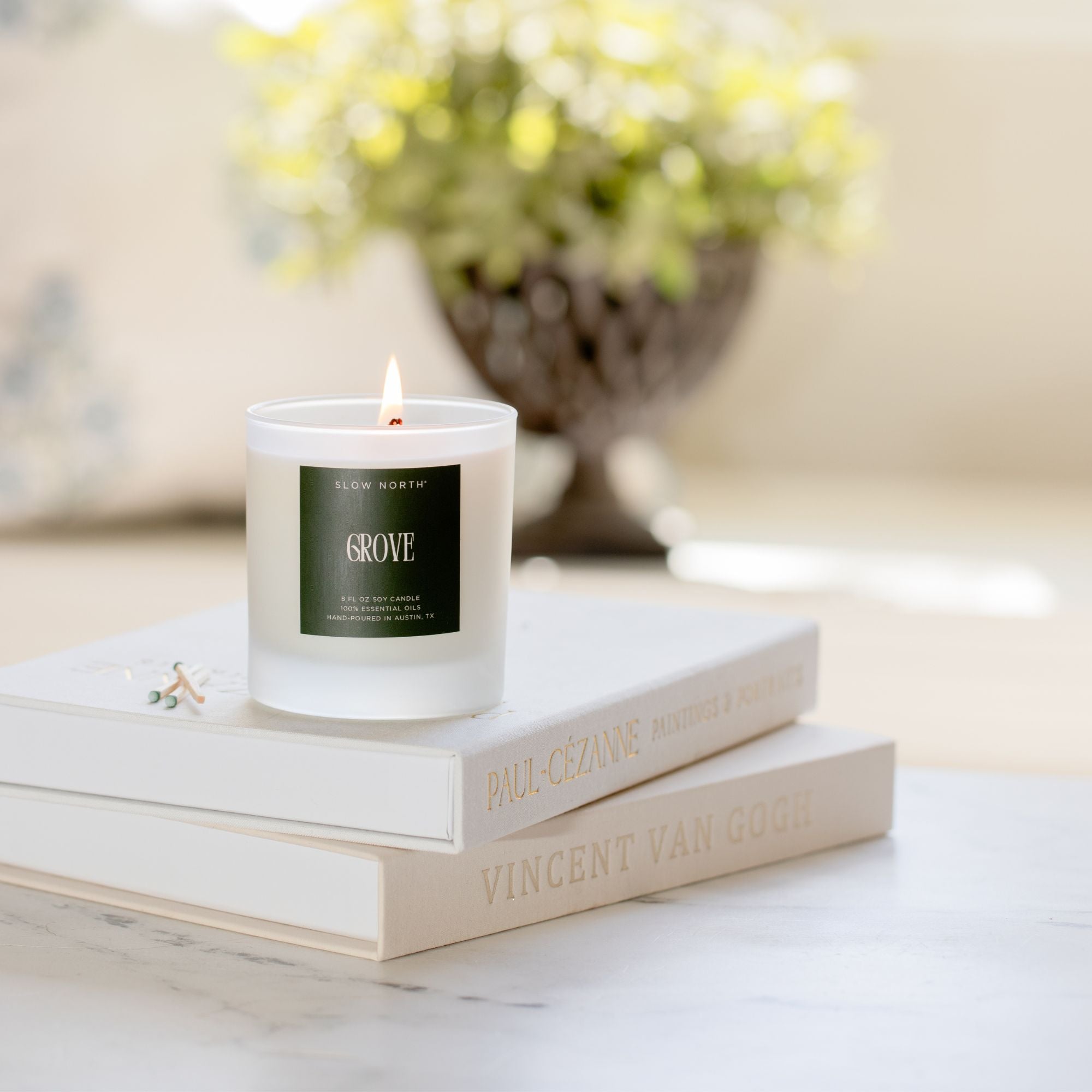 Candle on a stack of books with a blurred floral arrangement in the background