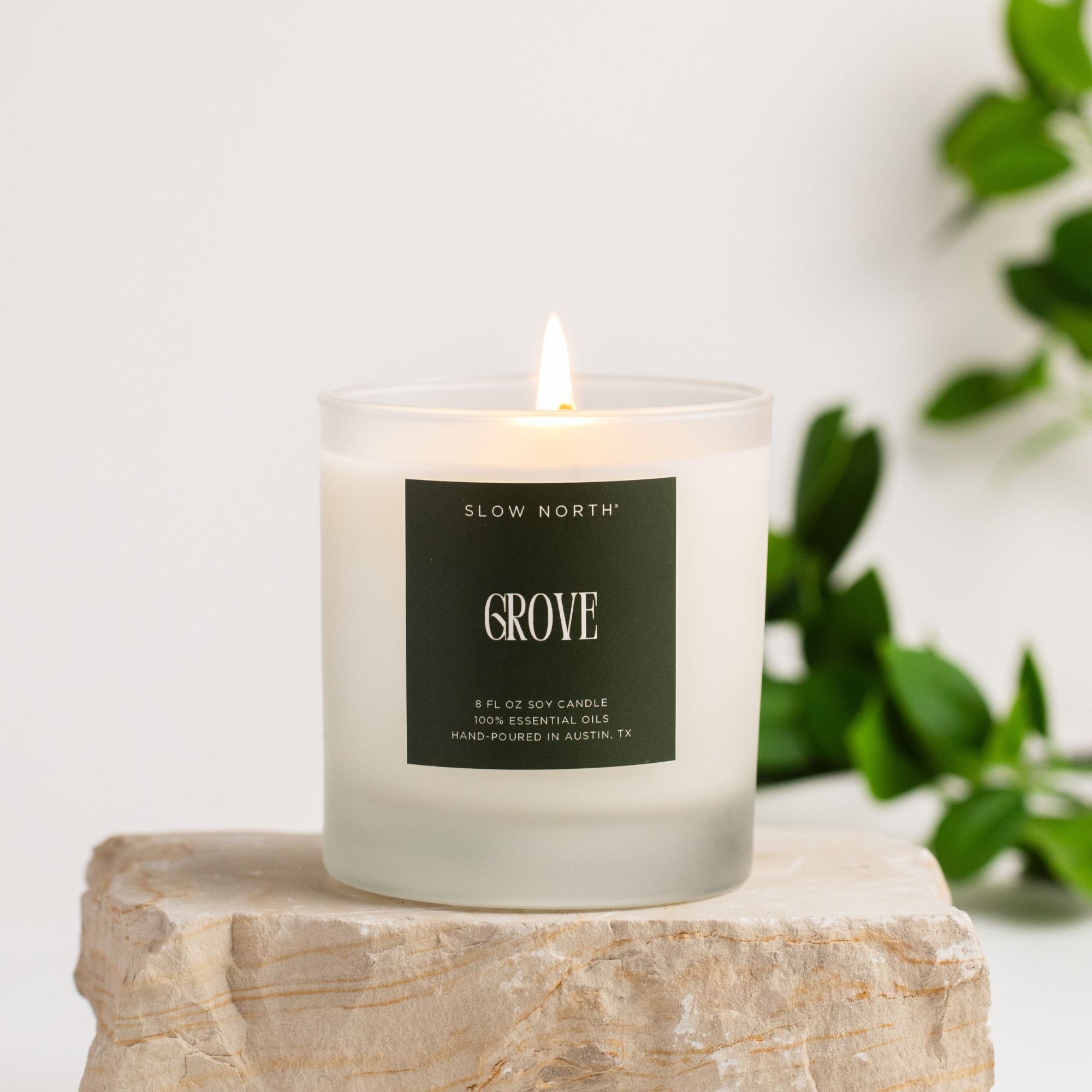 Candle labeled 'Grove' by 'Slow North' on a light surface with a blurred green plant in the background.