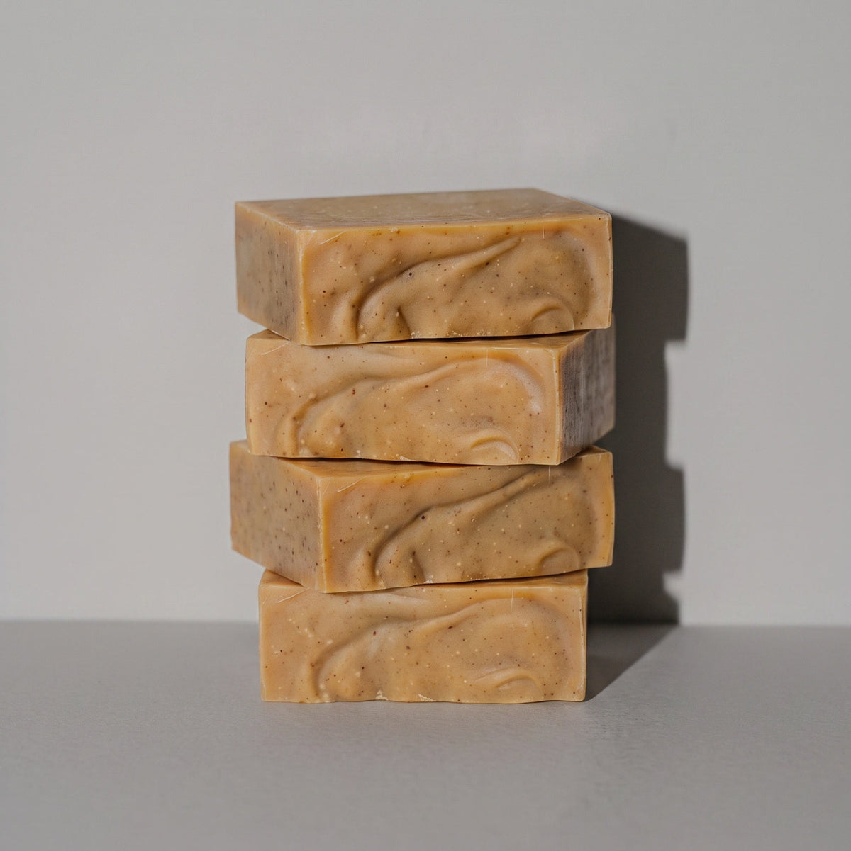 Four stacked rectangular bars of handmade soap in a warm tan and light brown marbled pattern, set against a plain light gray background.