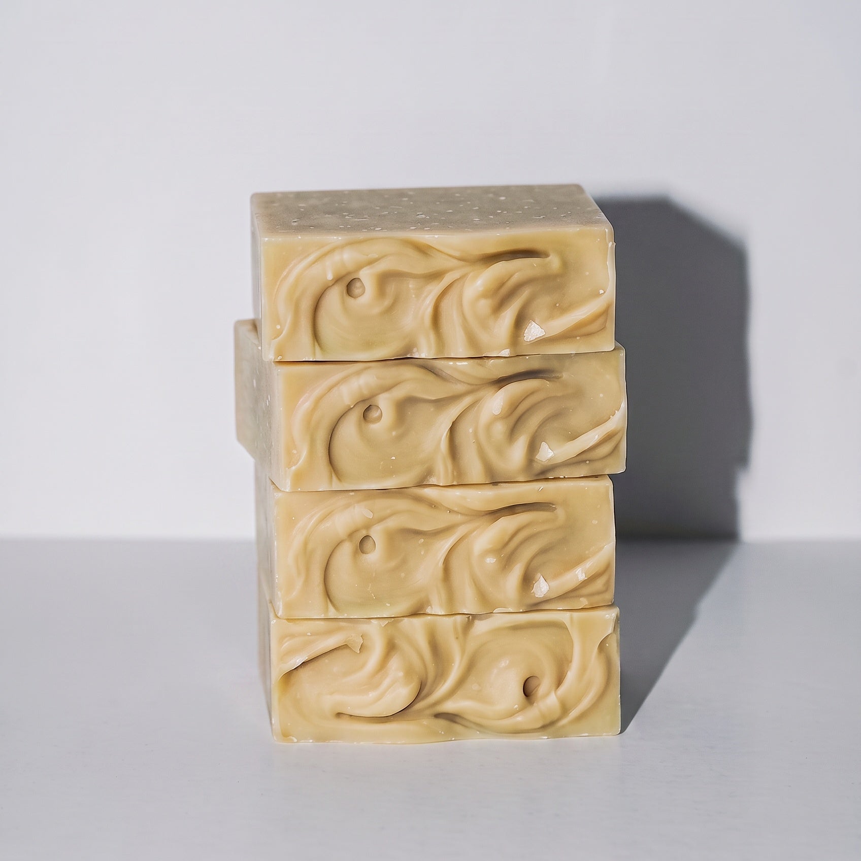 Four stacked rectangular bars of handmade soap in a warm cream-beige color, featuring a swirled embossed pattern on the front, set against a plain light gray background.