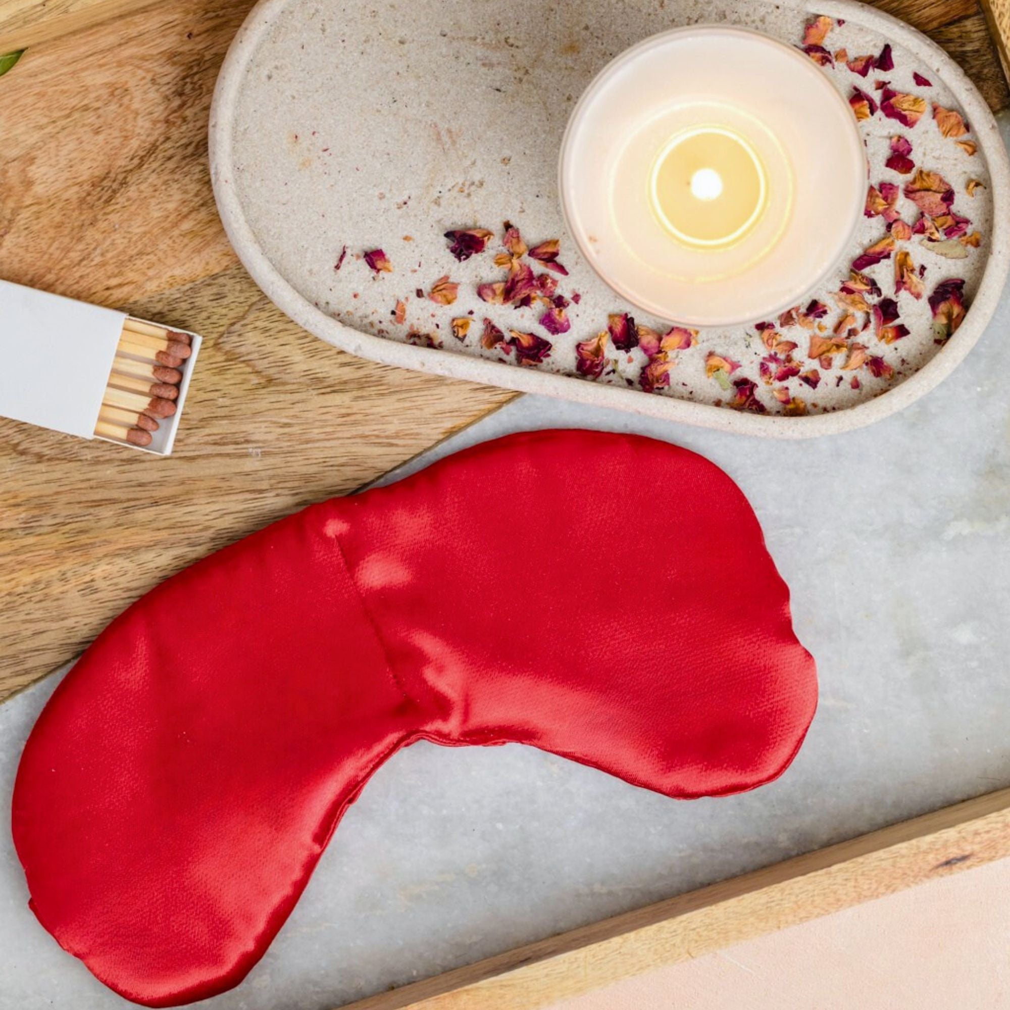 Red sleep mask on a marble surface with a lit candle and matches in the background.
