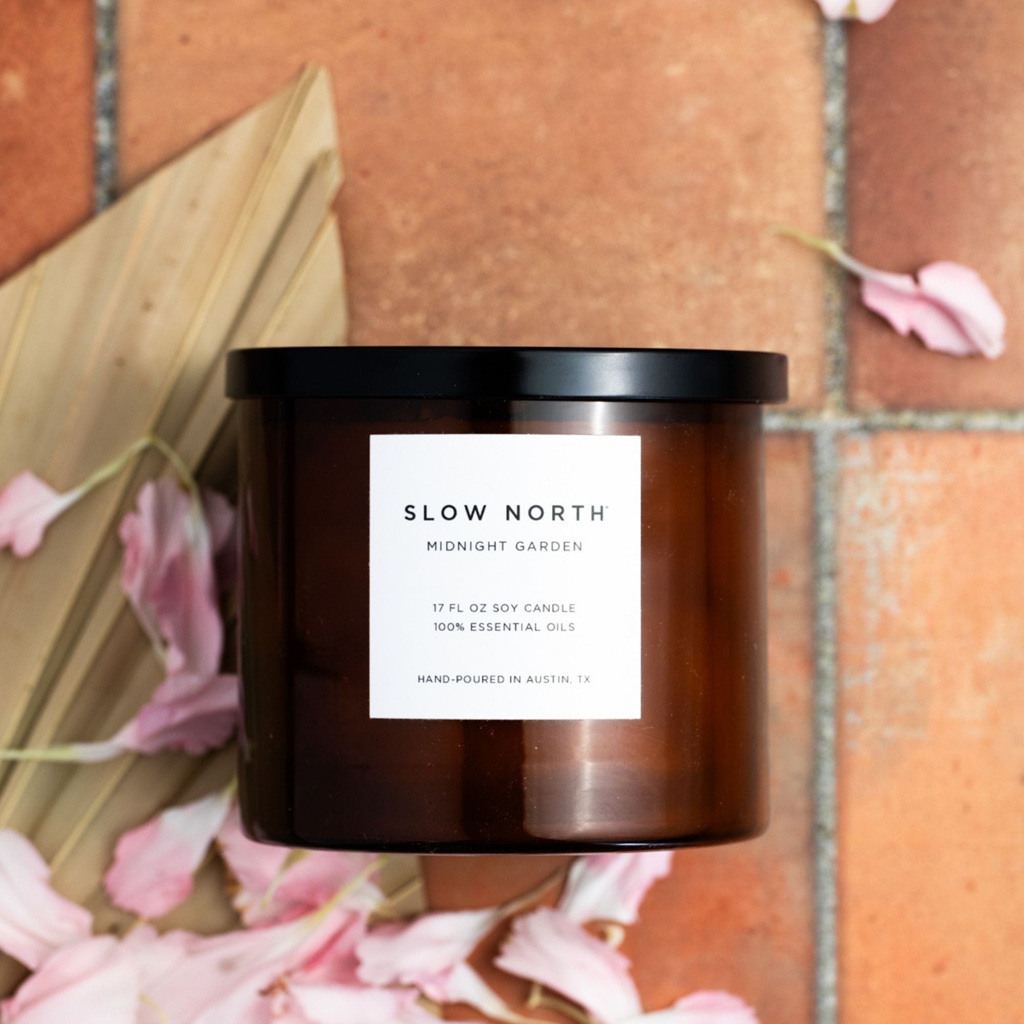Brown candle with a white label on a brick surface with pink flowers