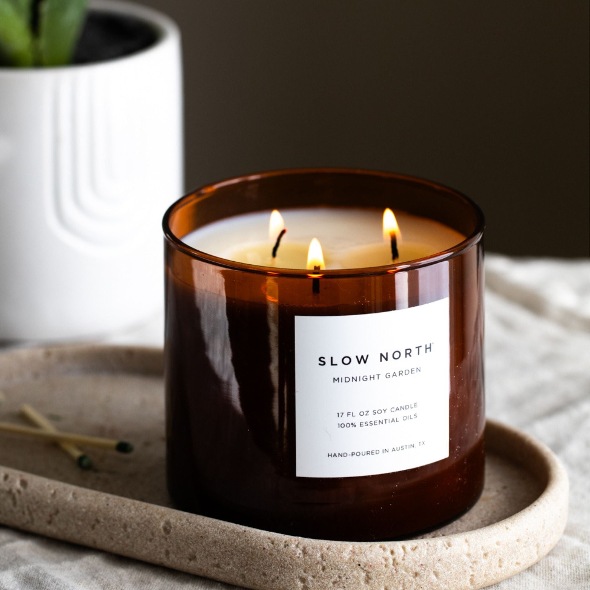 Non-Toxic Candle with 'Slow North' label on a stone surface with a plant in the background