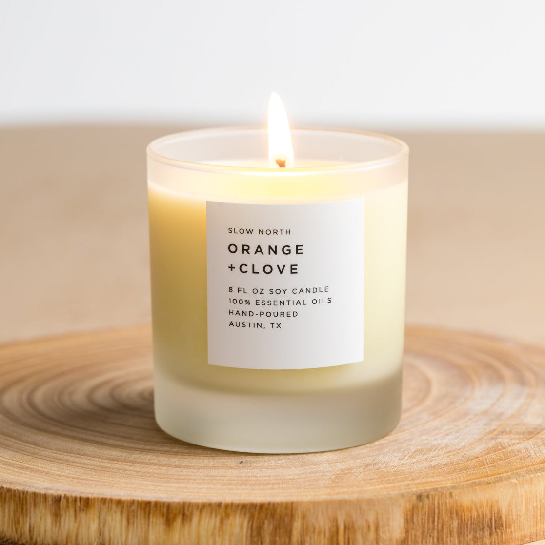Candle labeled 'Orange + Clove' on a wooden surface with a neutral background