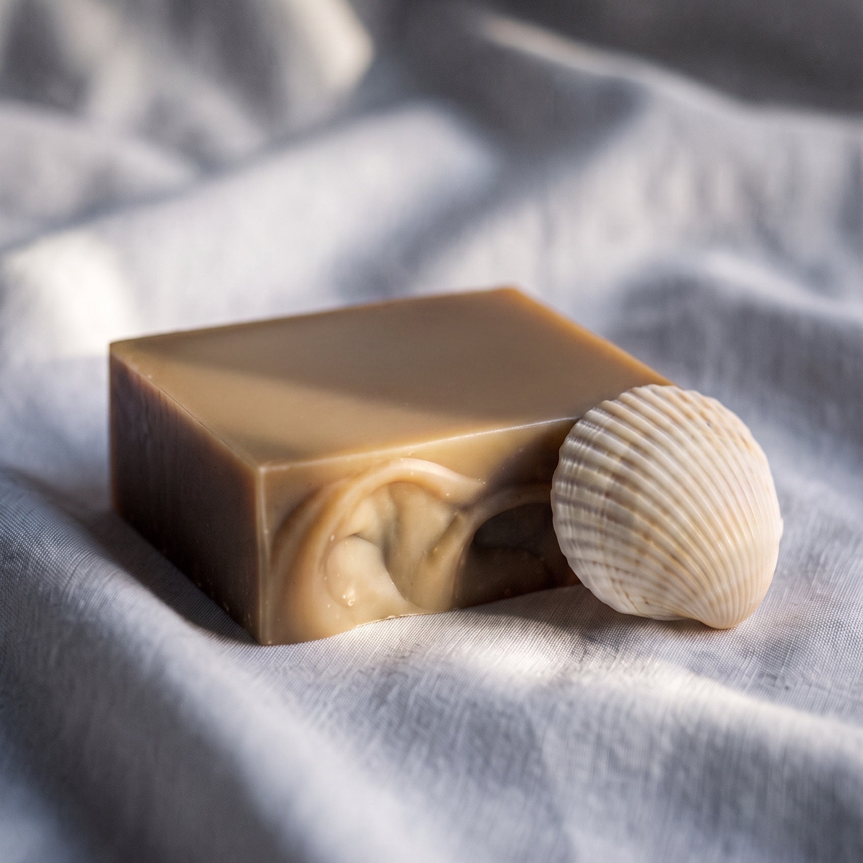 bar of natural soap with seashell propped against it on a white linen towel