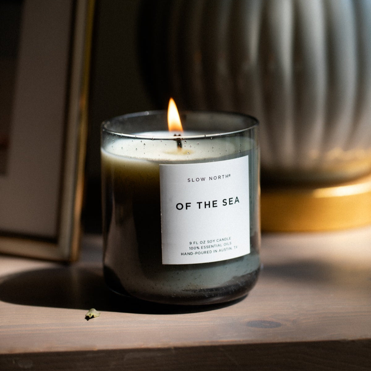 Candle labeled 'Of the Sea' on a wooden surface with a blurred background
