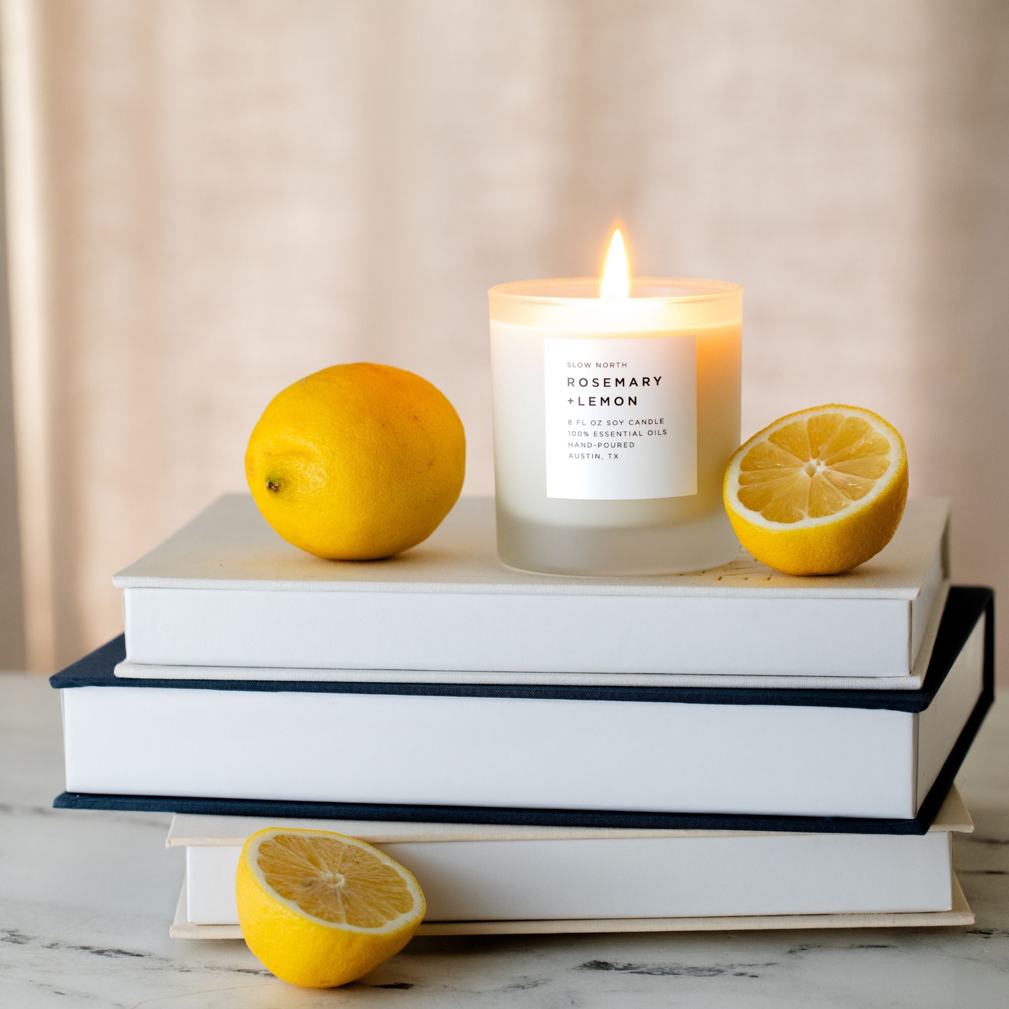 Candle with lemons on books against a neutral background