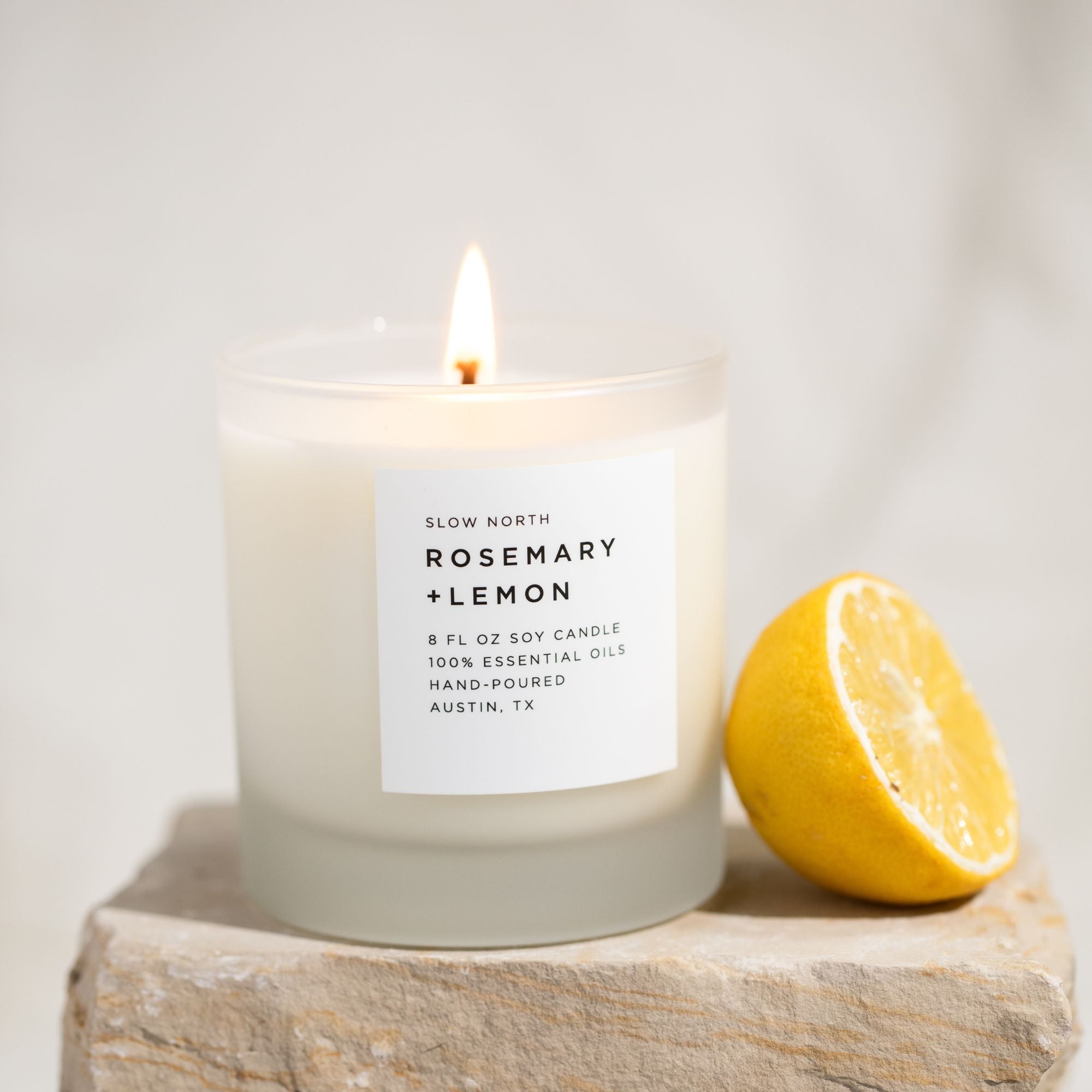 Candle labeled 'Rosemary + Lemon' next to a lemon on a light background