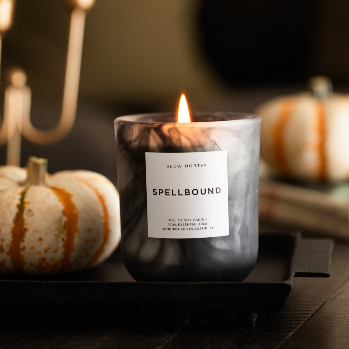 Candle labeled 'Spellbound' with pumpkins and a chandelier in the background Halloween candle
