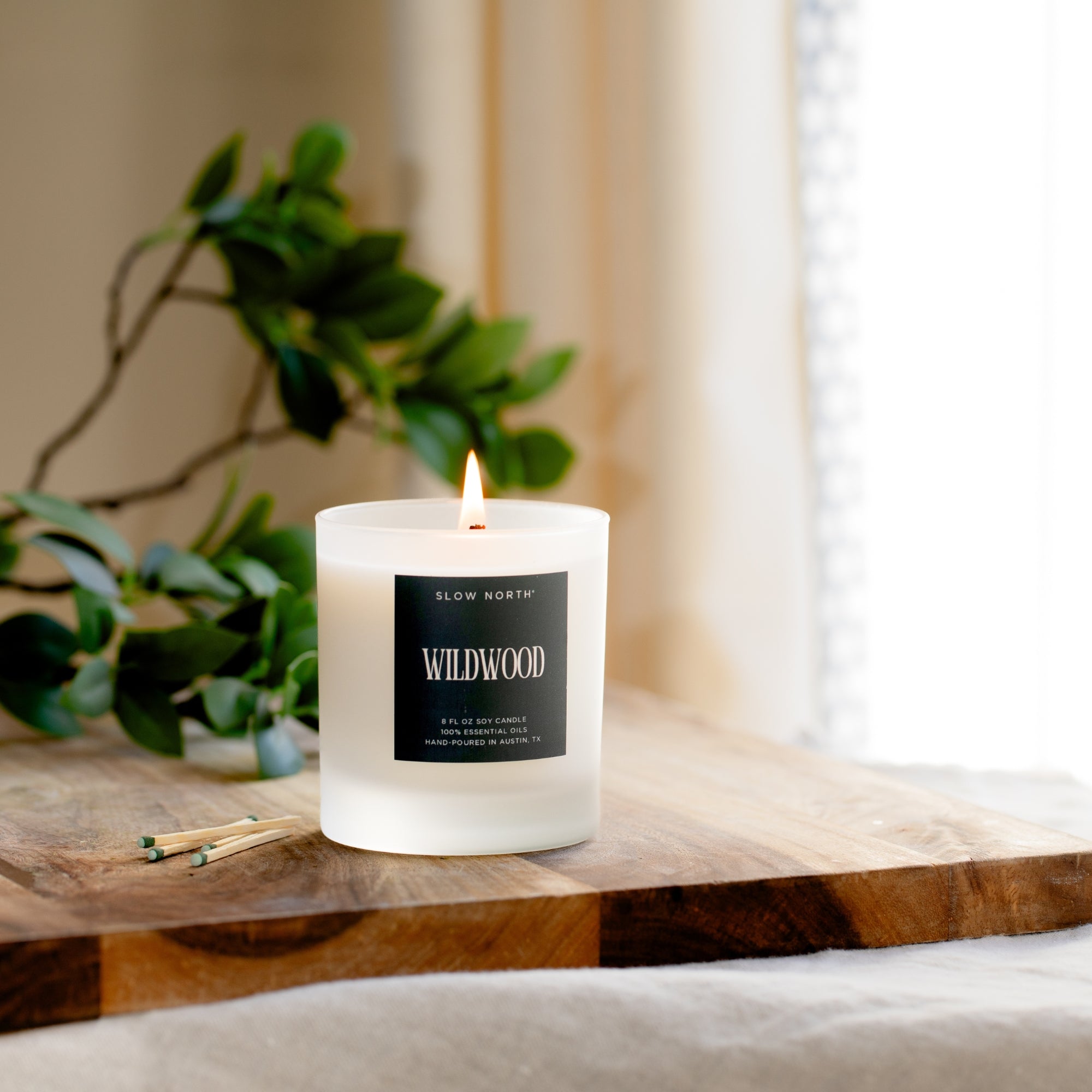 Candle labeled 'Wildwood' on a wooden surface with a plant in the background