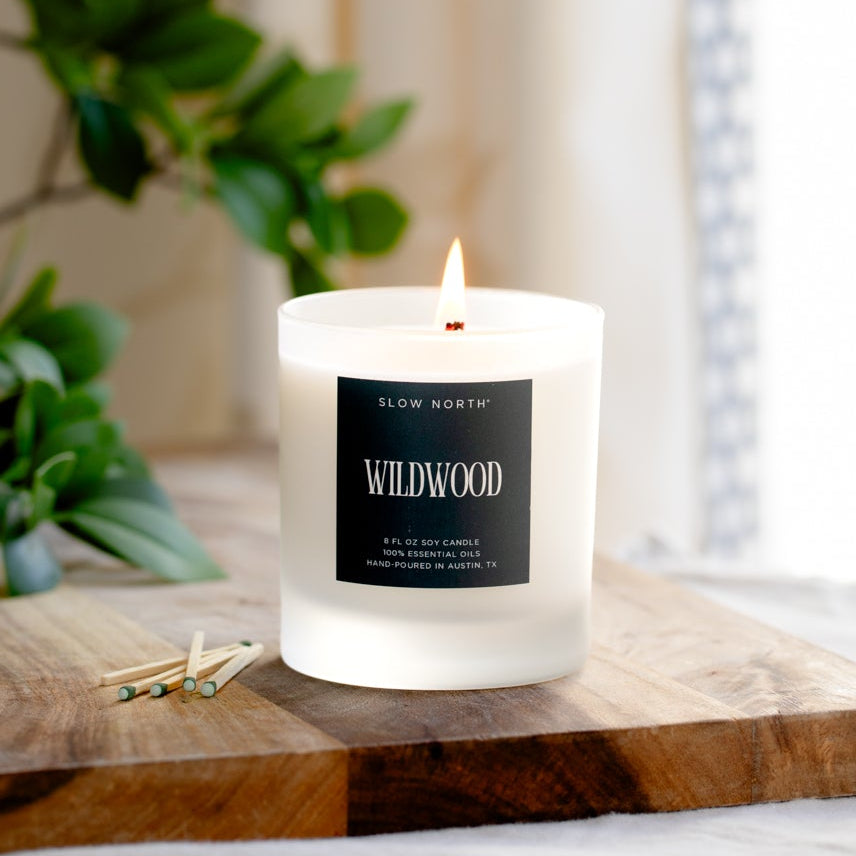 White candle with a label on a wooden surface near a window with curtains.