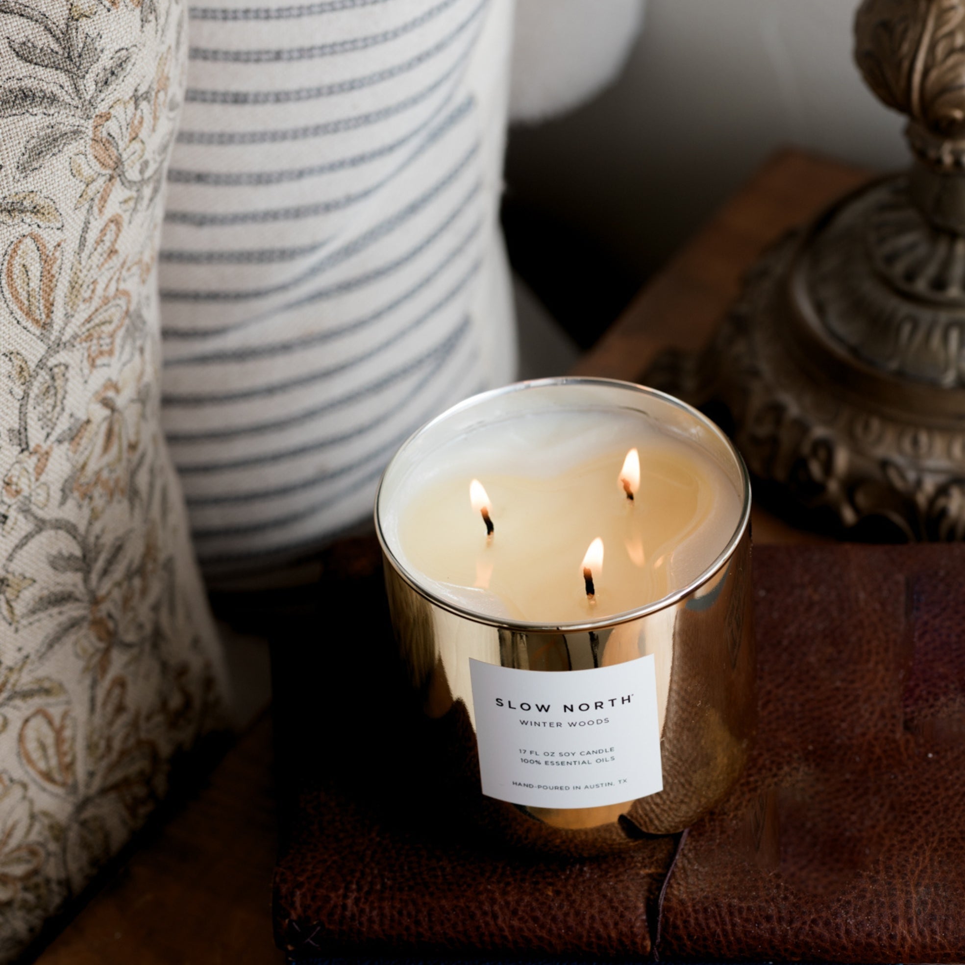 Candle with 'Slow North' label on a surface with decorative items in the background