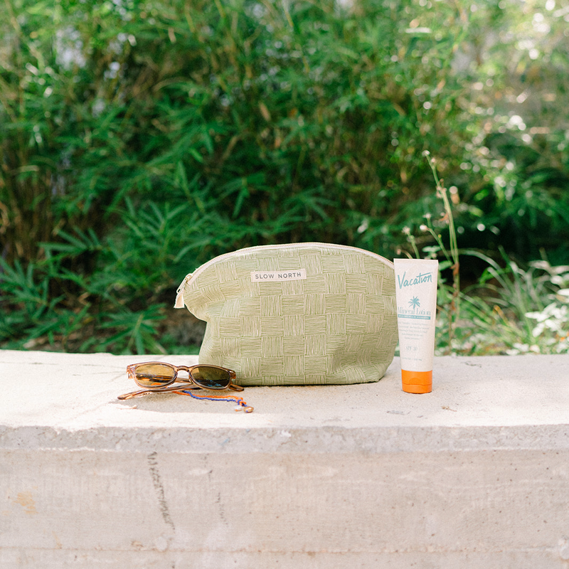 handcrafted green cosmetic zipper bag next to Vacation sunscreen and sungasses